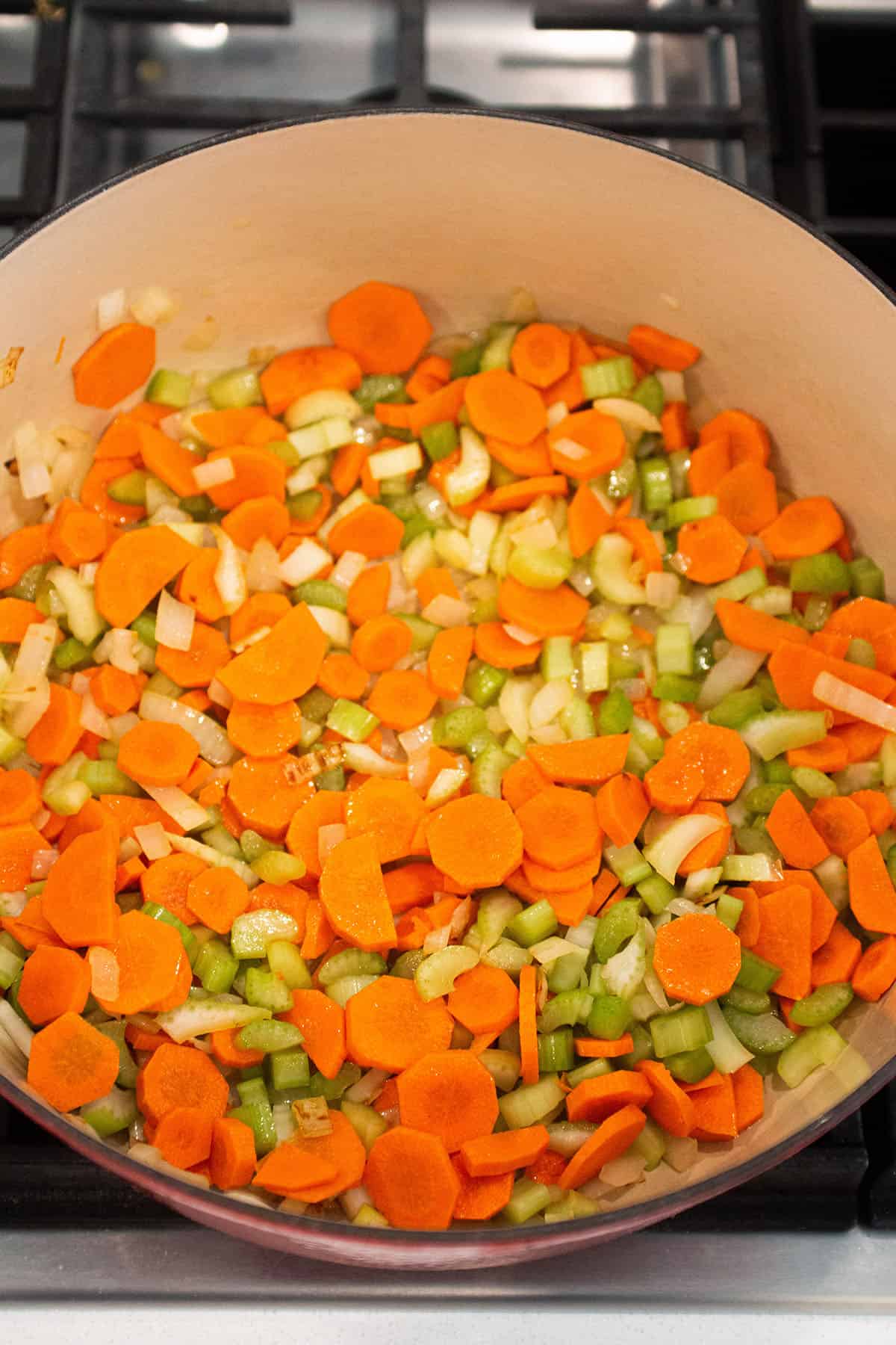 A large Dutch Oven with onions, carrot and celery sautéing in olive oil.