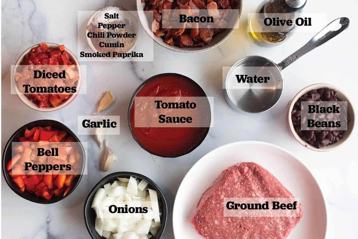Ingredients in prep bowls to make chili. Ground beef, onion, tomatoes, tomato sauce, spices, garlic, bacon, olive oil, black beans and water.