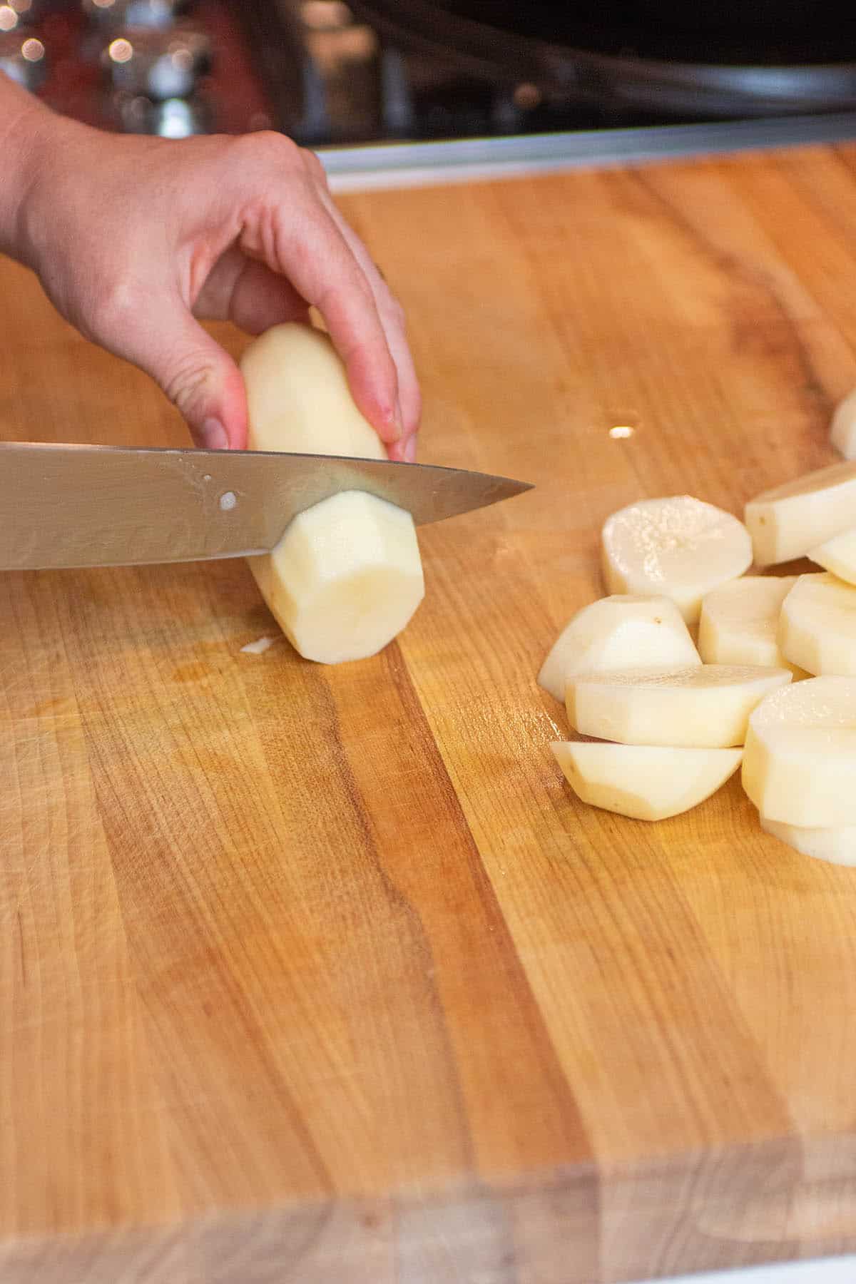 A cutting board with peeled potatoes being cut into pieces.