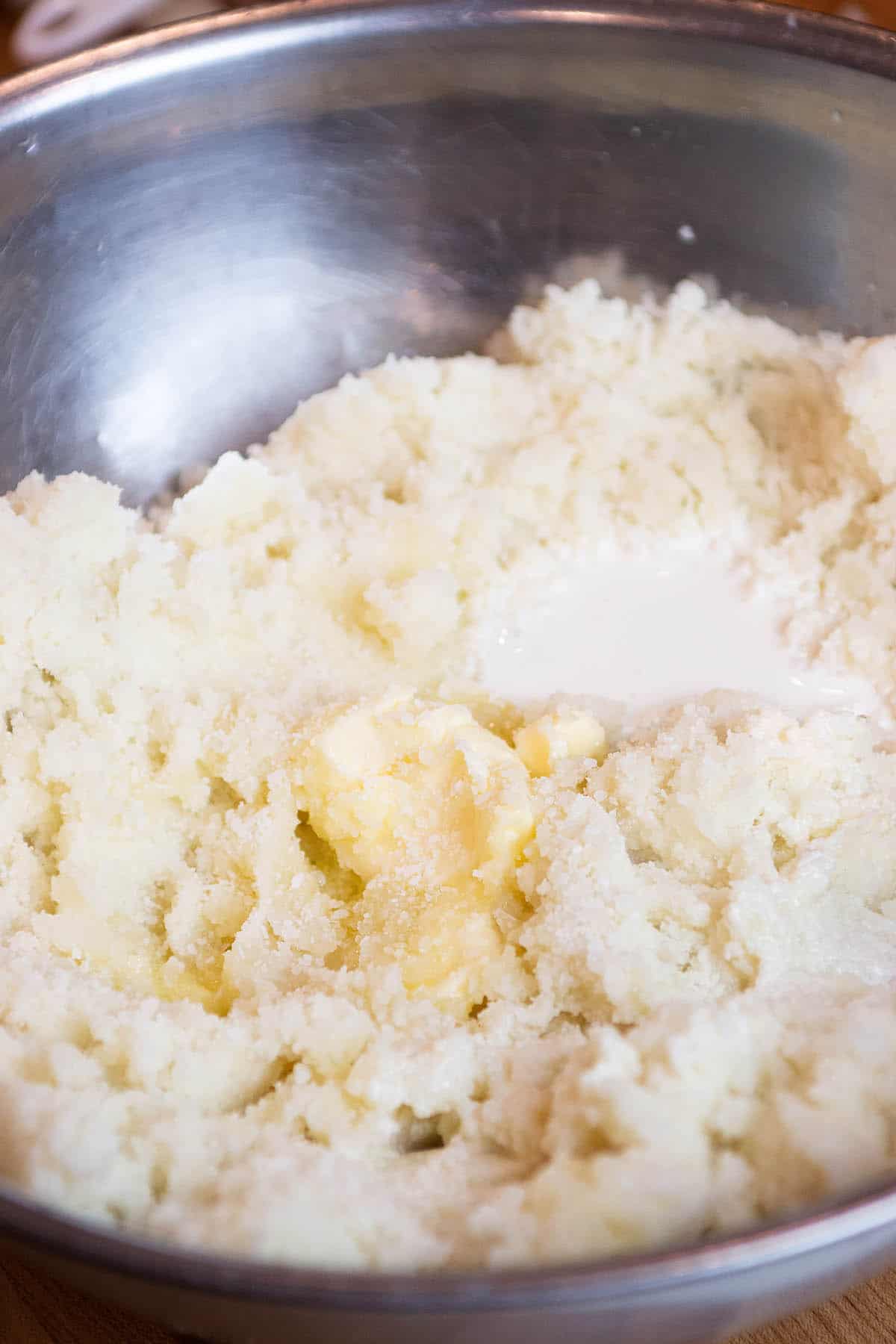 A large mixing bowl with mashed potatoes, butter and cream.