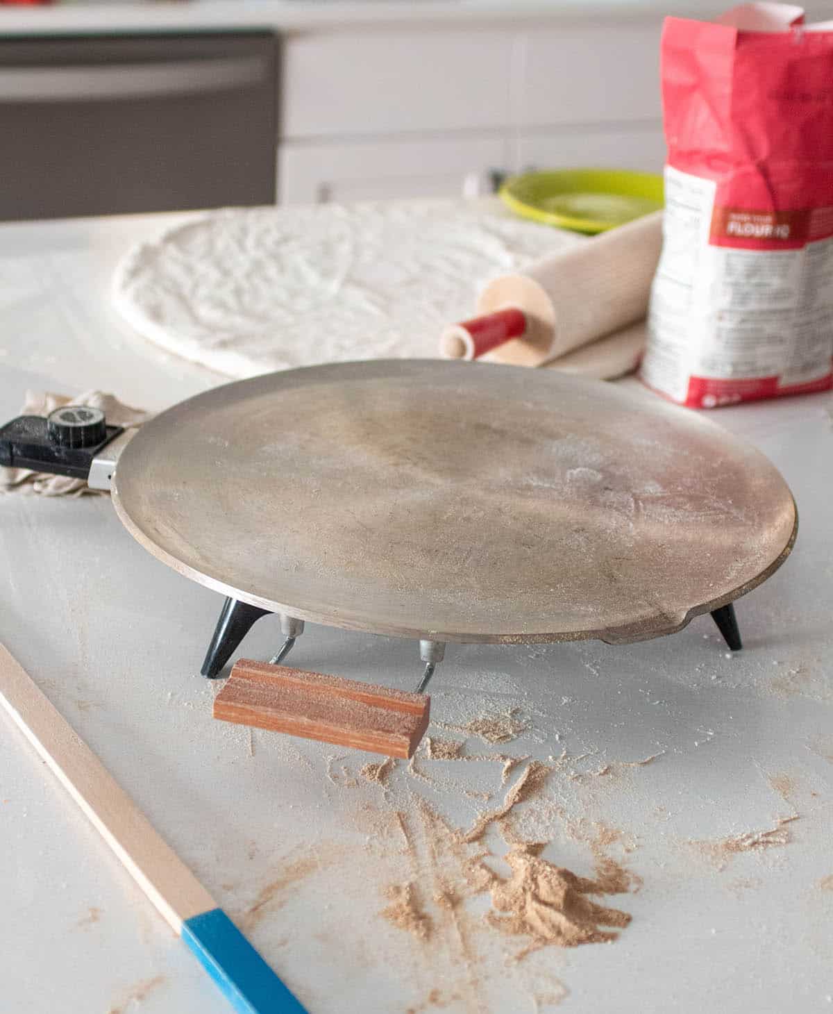 Lefse workstation with a griddle, rolling pin, turning stick, and a bag of flour.