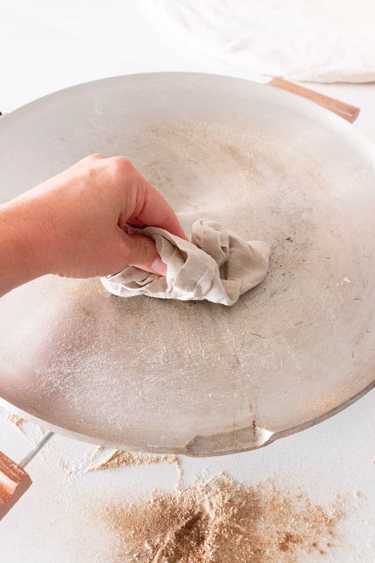 A hand with a dry cloth wiping burn flour off a lefse griddle.