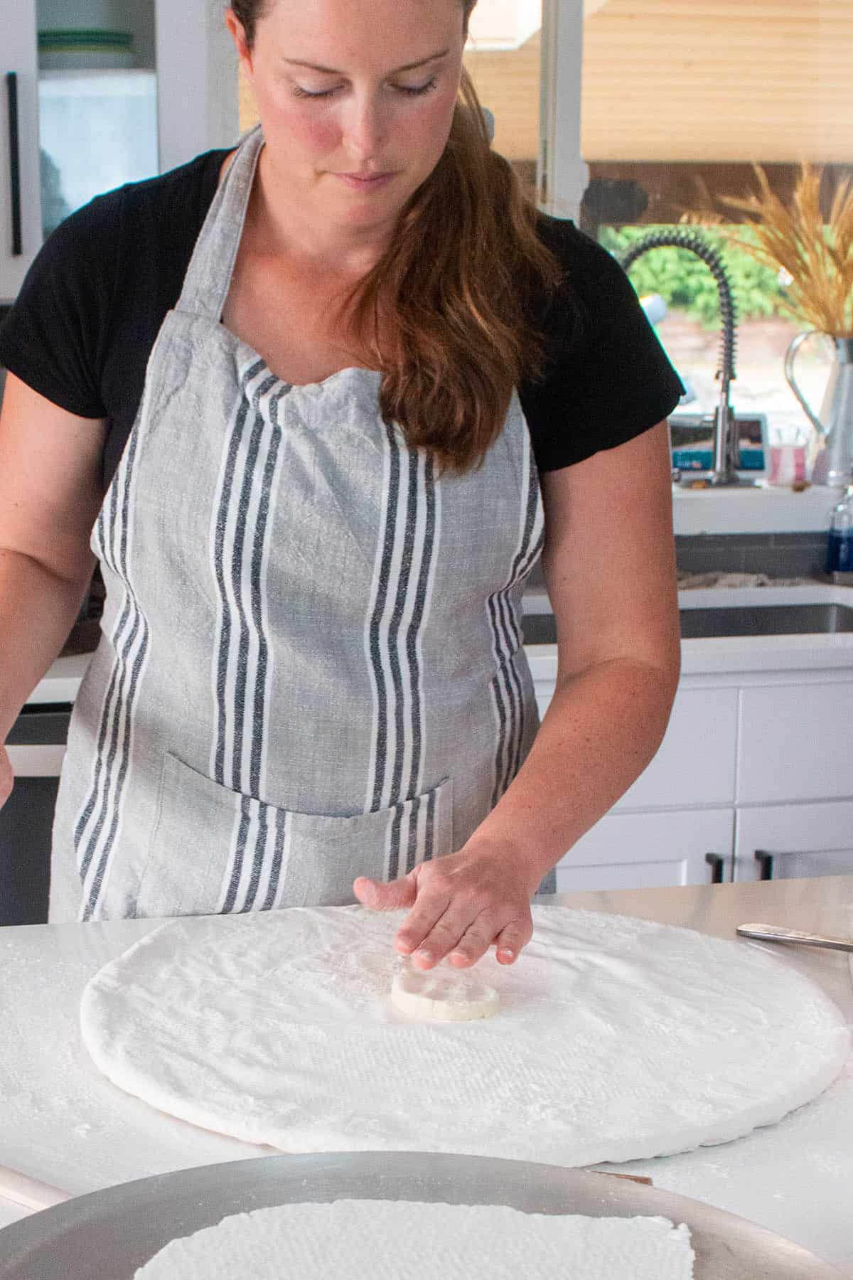 A baker with a piece of lefse dough rolling it in flour.