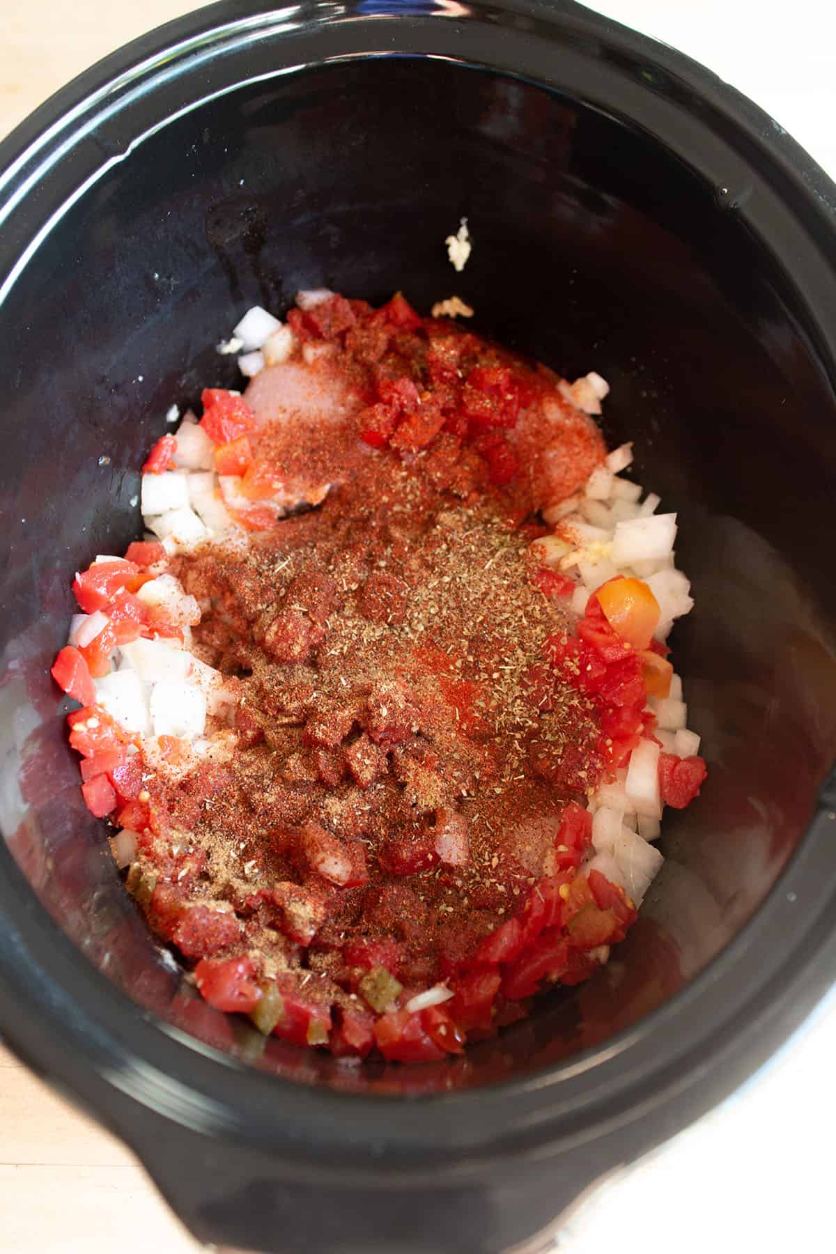 A crockpot full of raw chicken, onions, diced onions and spices.