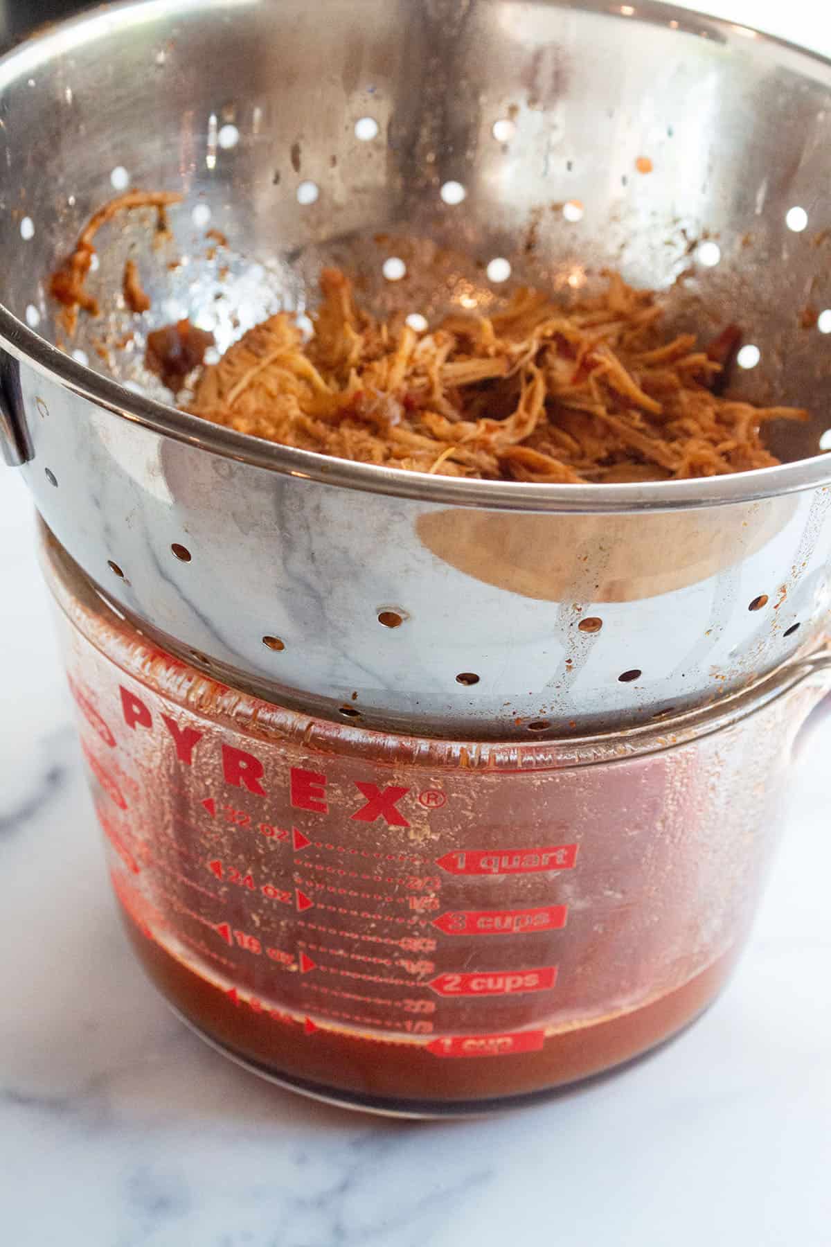 A pyrex glass liquid measuring cup with a strainer on top separating chicken from the juice.