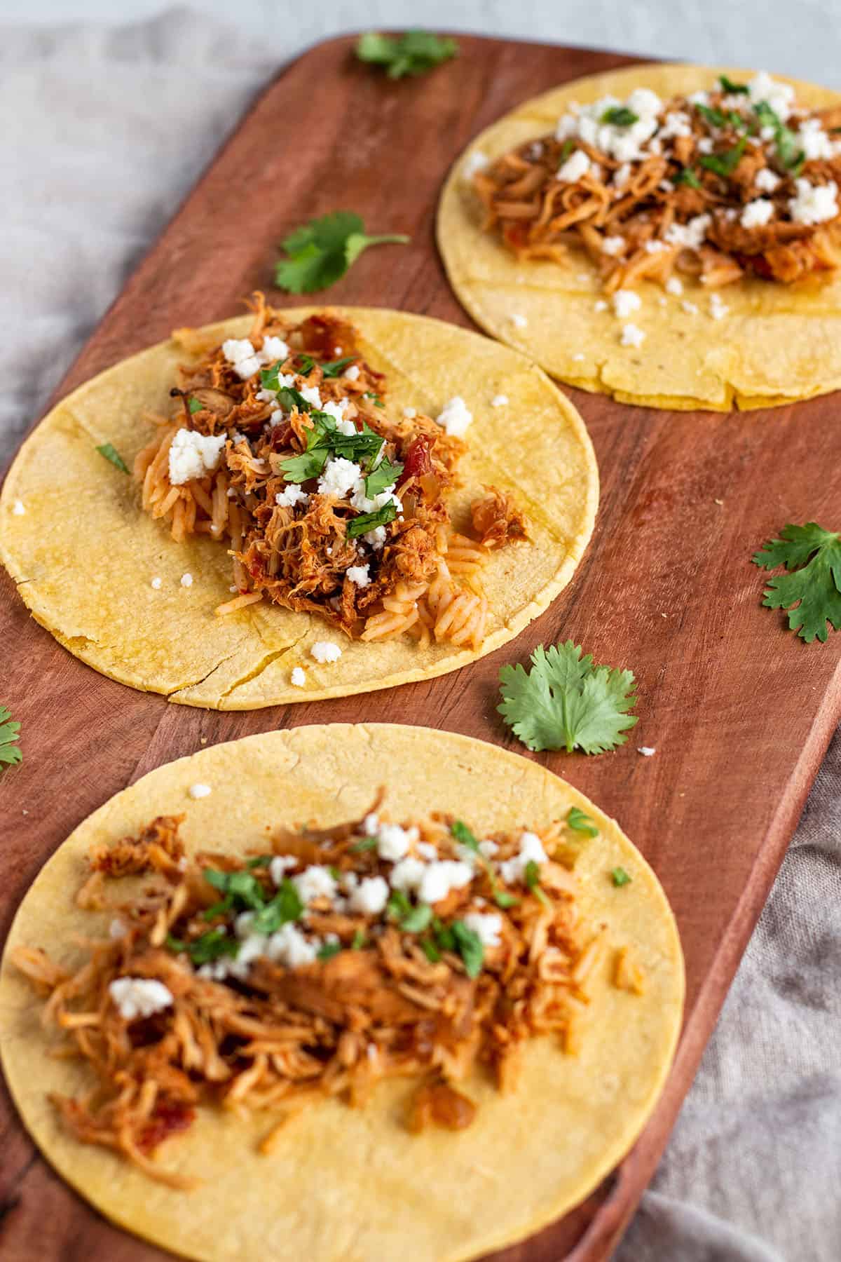 A wooden board with three corn tortillas with shredded chicken on top.