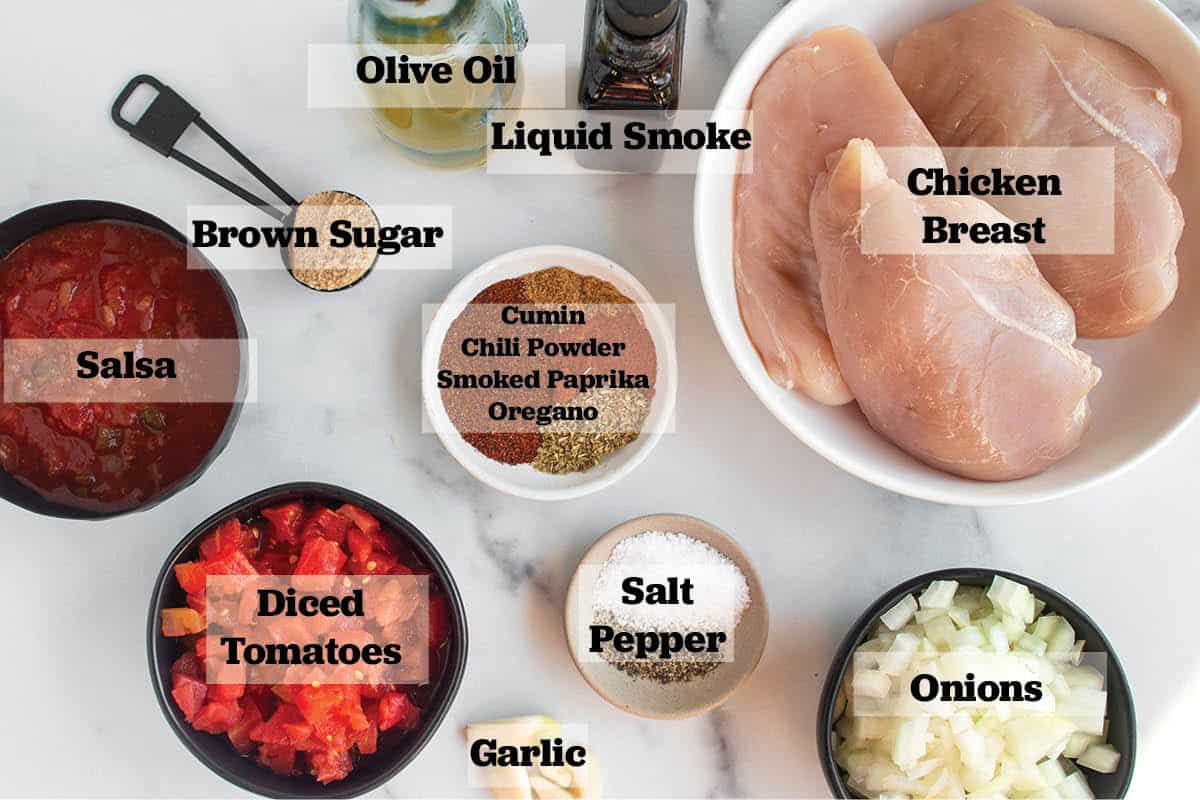 Ingredients all laid out in bowls. Chicken, liquid smoke, olive oil, brown sugar, salsa, diced tomatoes, garlic, onions, salt, pepper, and spices.