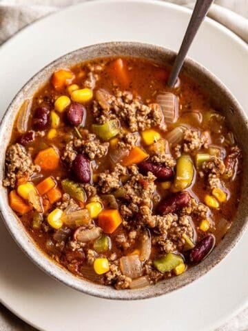 A bowl of soup filled with ground beef and veggies.
