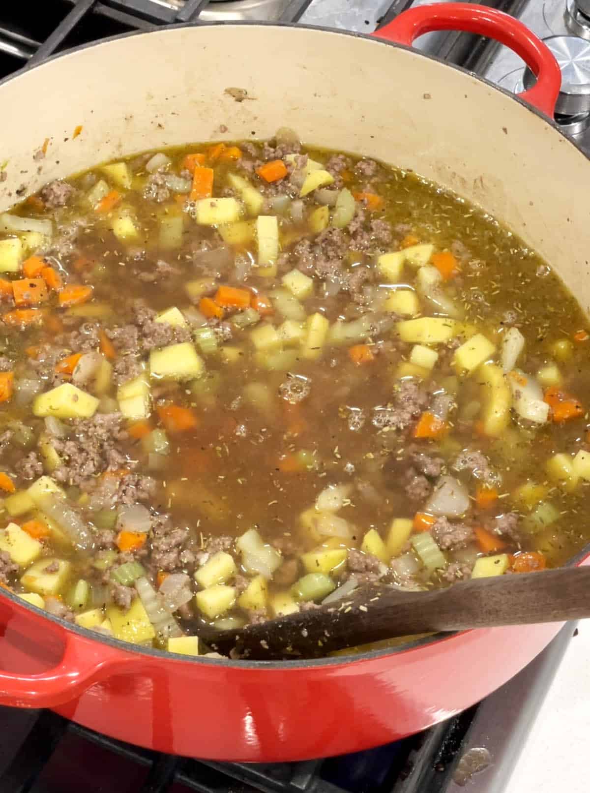 Veggies and grond beef simmering in a beef stock in a large Dutch Oven.