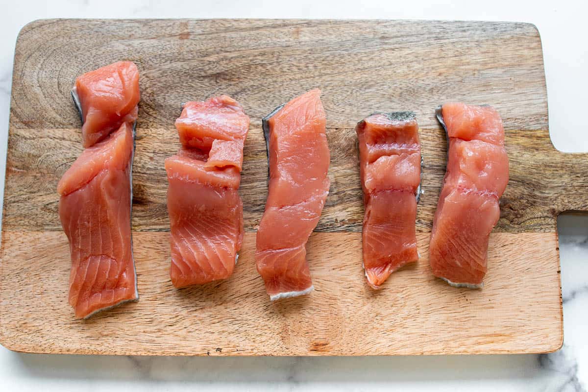 A wooden cutting board with pieces of fresh salmon fillet.