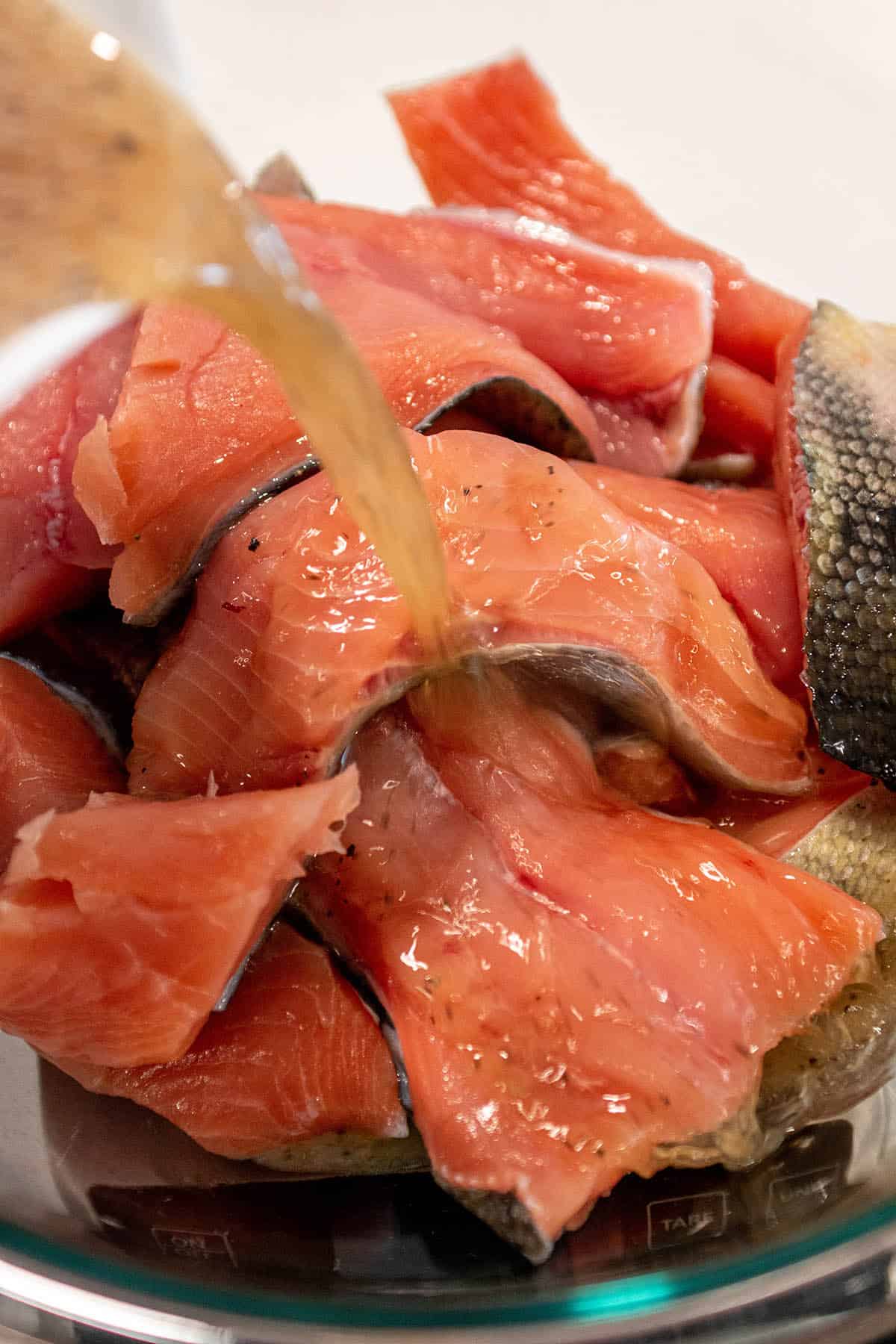 A glass bowl with pieces of salmon filet with a brine mix being poured over the top.