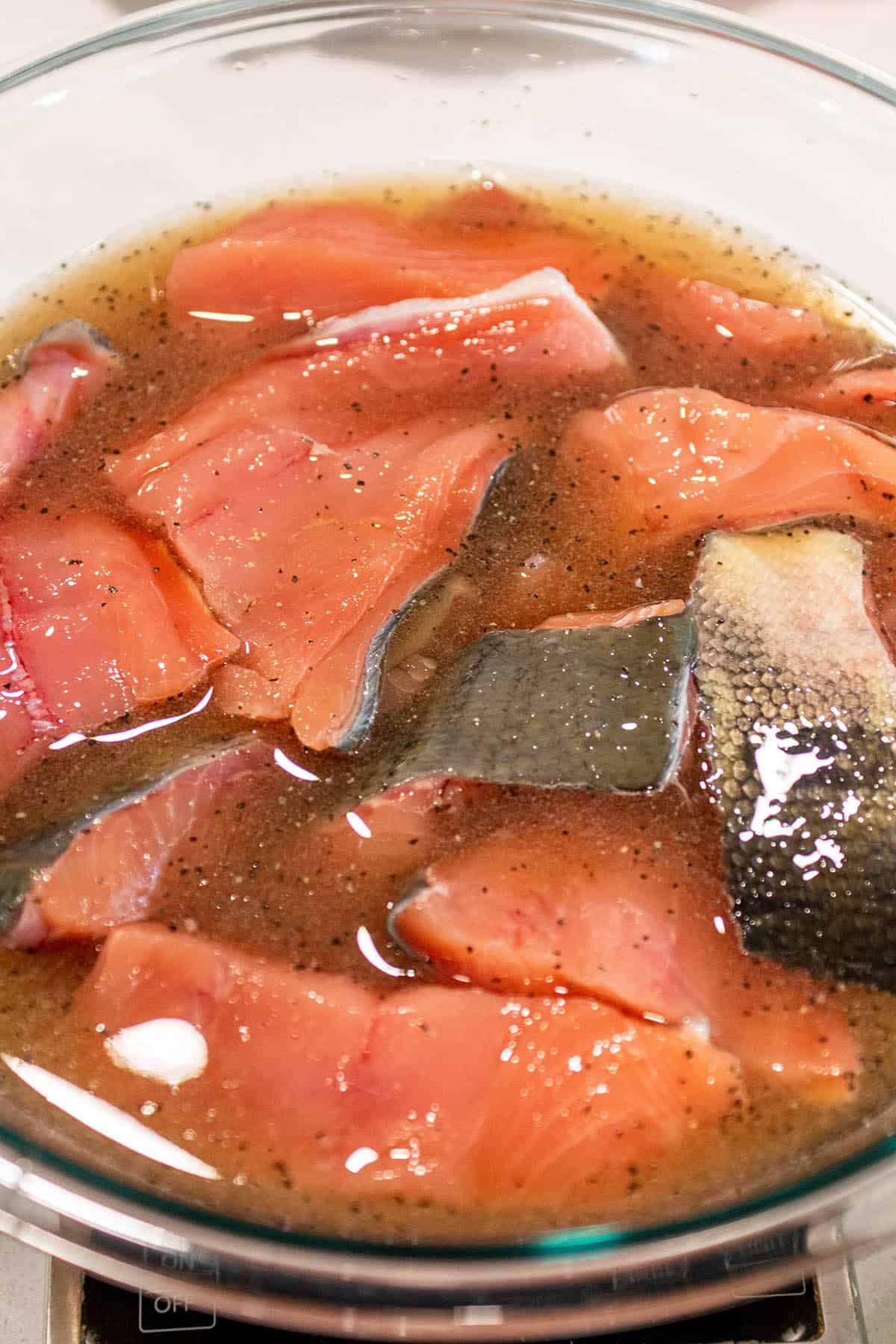A glass bowl with salmon filets sitting in a brine solution.