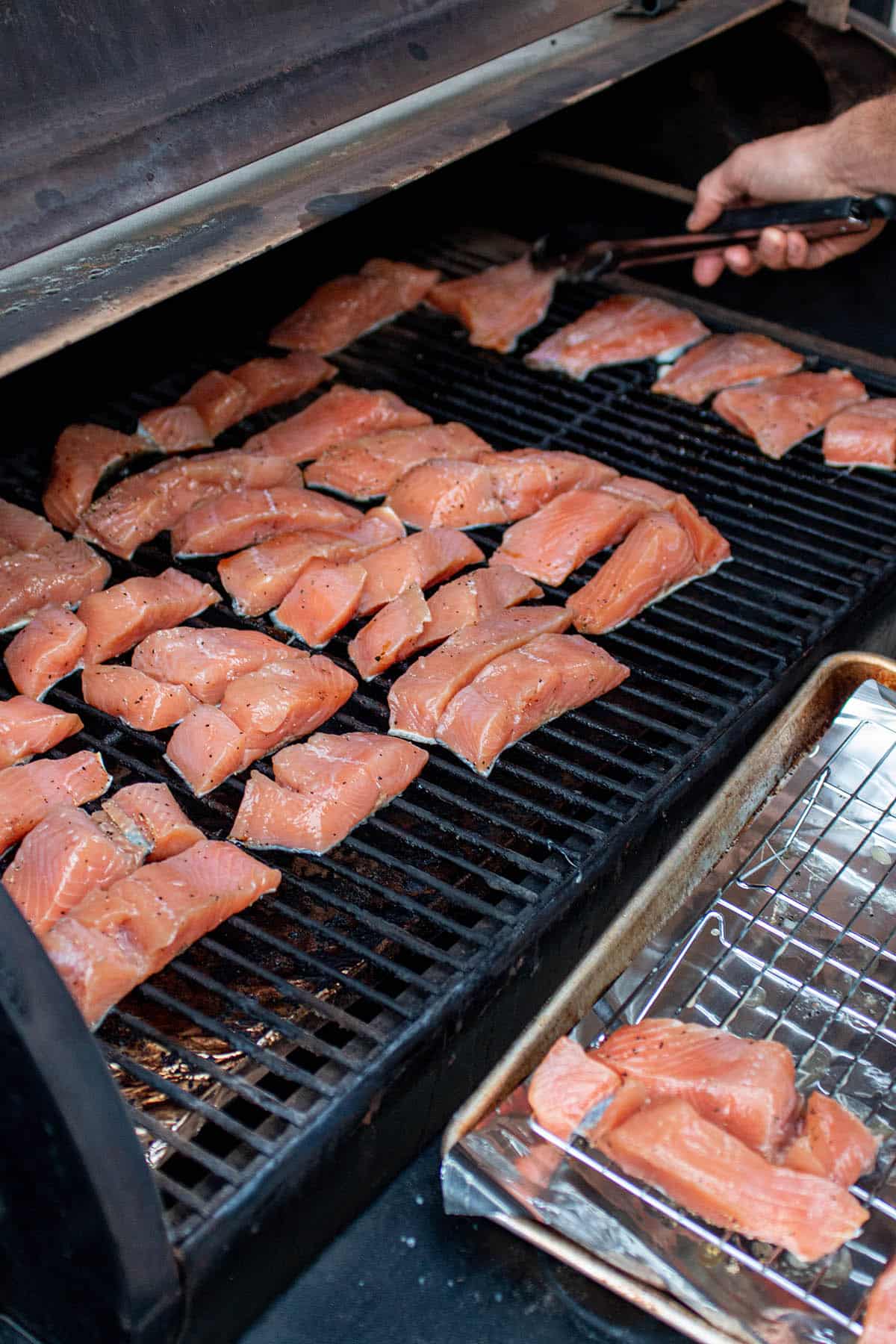 A Traeger grill with lots of pieces of salmon being placed on the grill grates. 