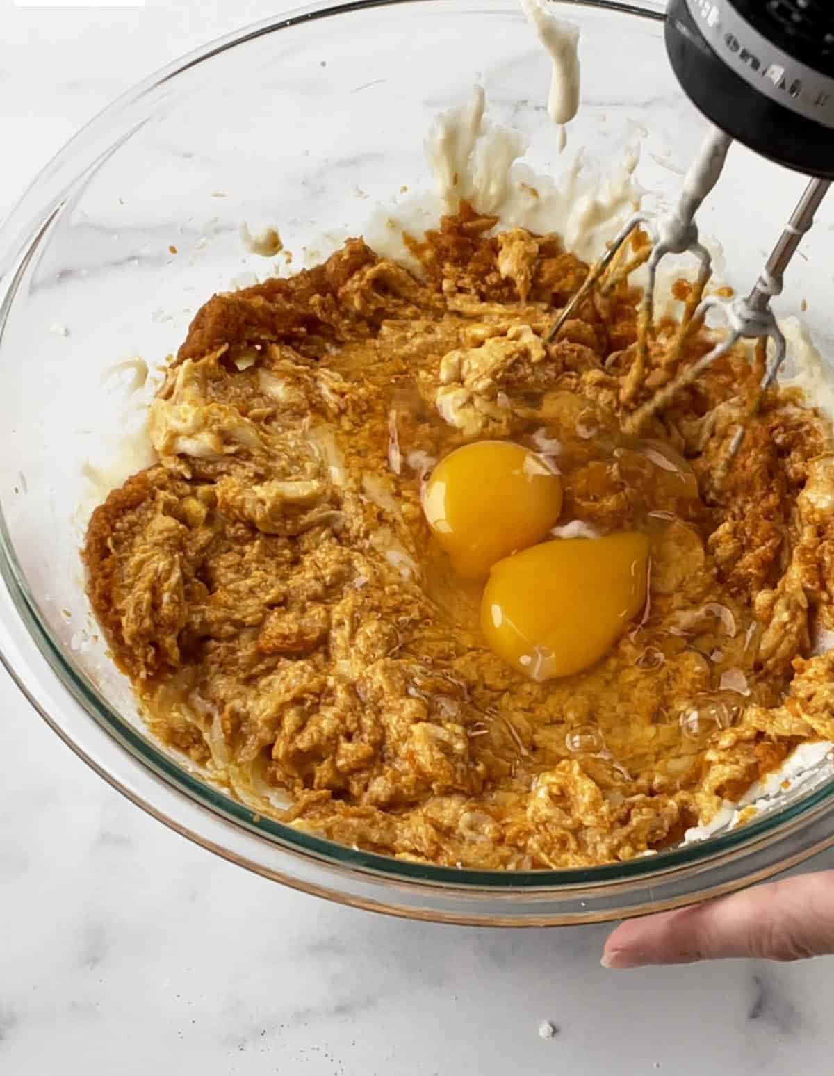 A glass bowl with a pumpkin batter and two eggs being whisked in.