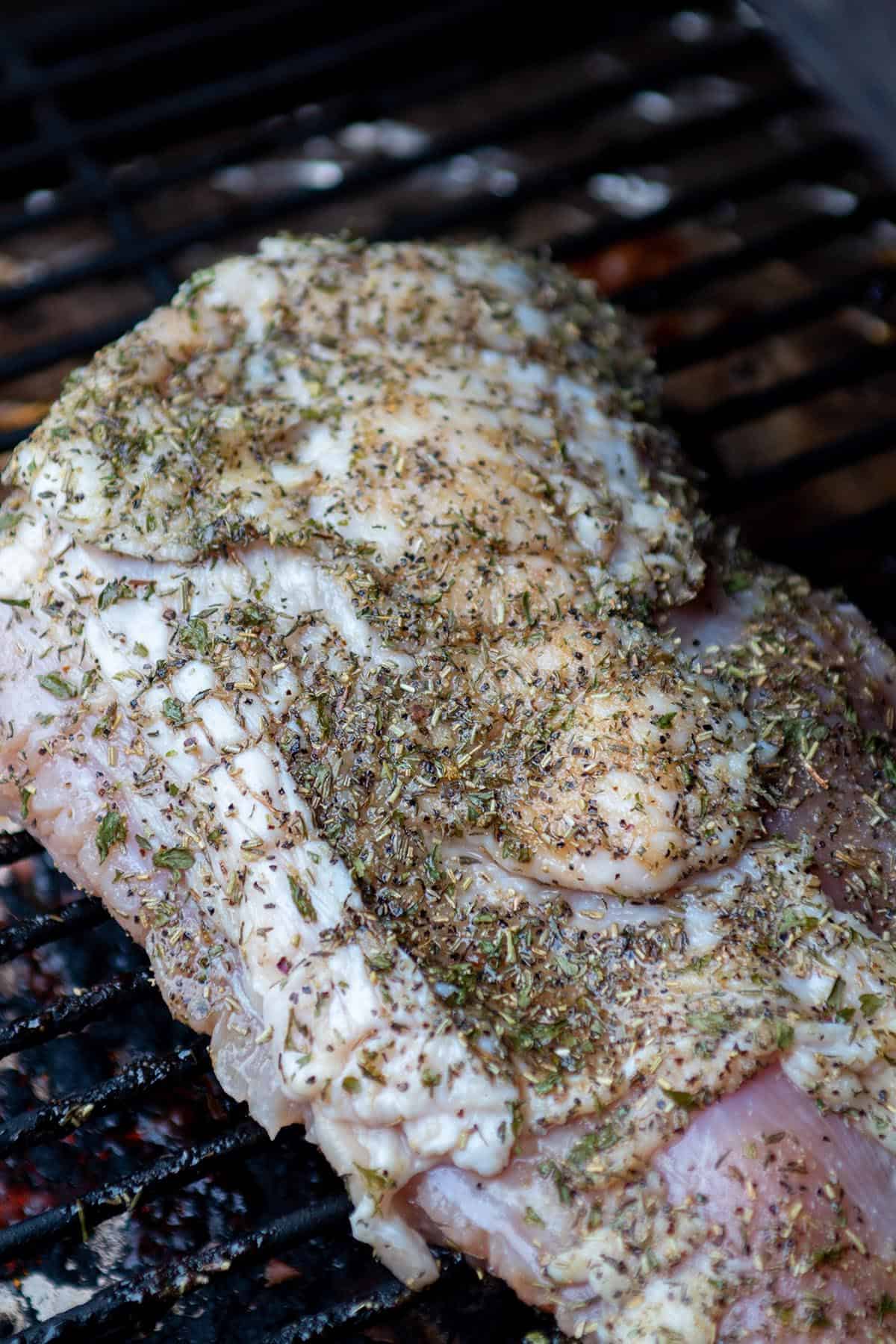 A raw turkey breast with a dry rub sitting on a Traeger grill. 