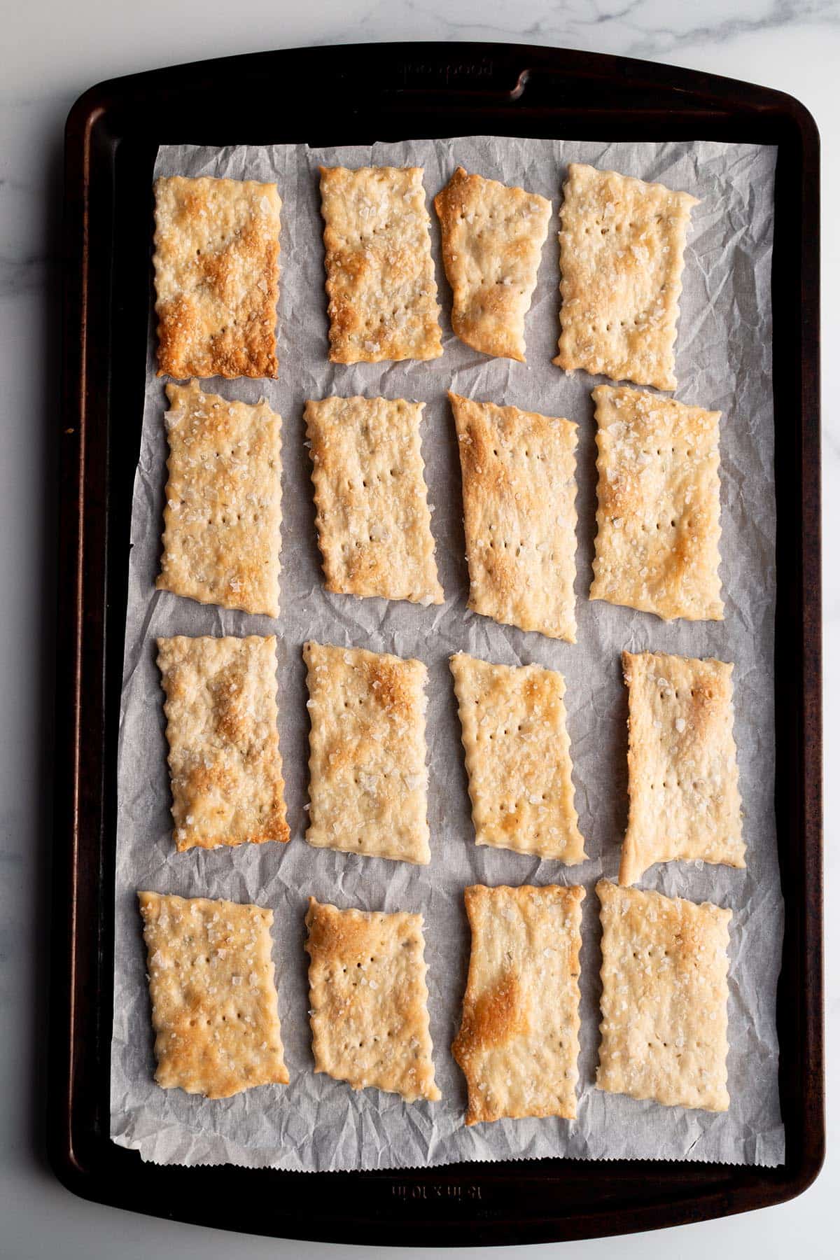 Baking pan with parchment paper and rectangle sourdough crackers.