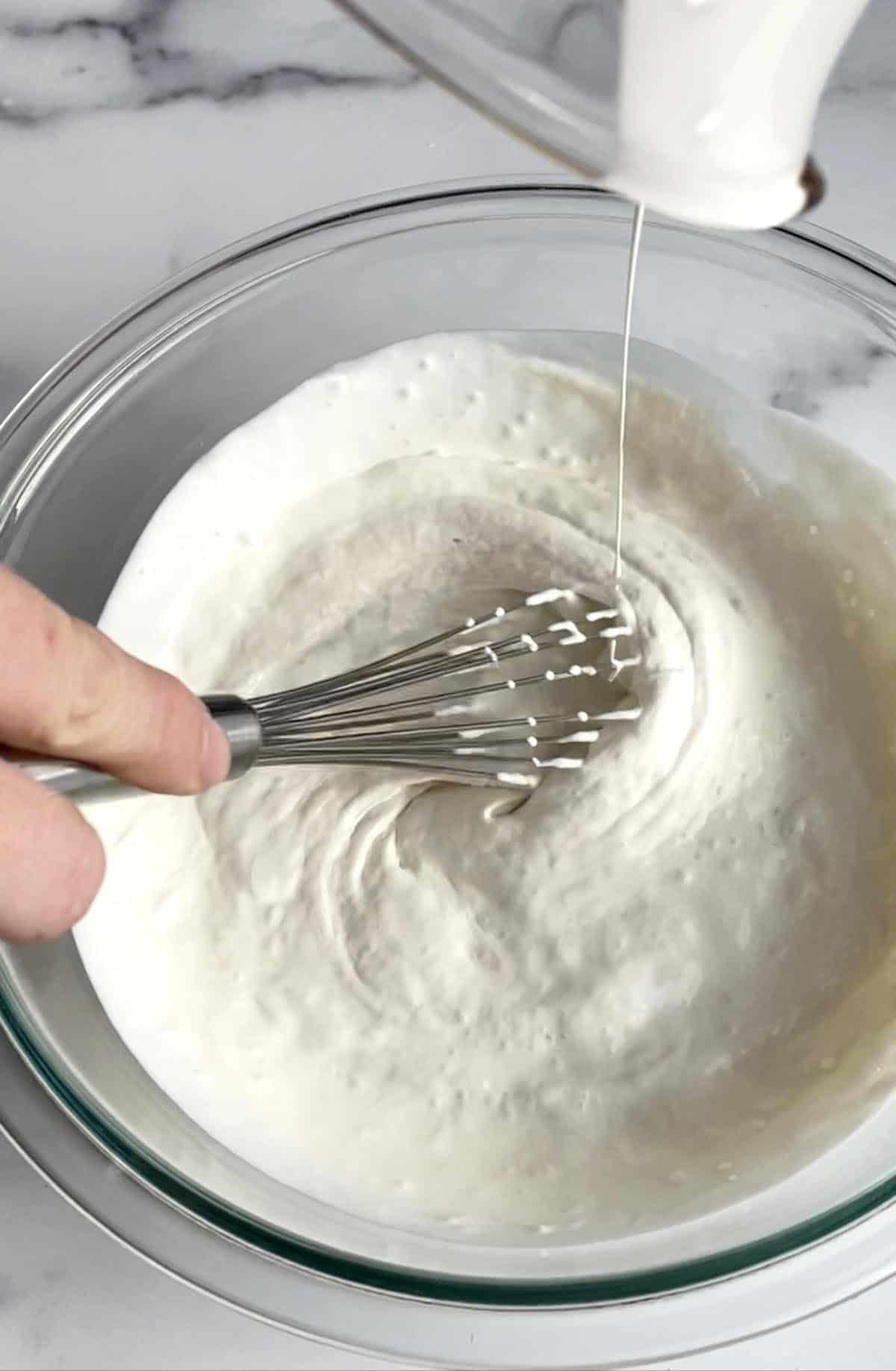 A glass bowl with a hand whisking cream and sourdough starter together. 