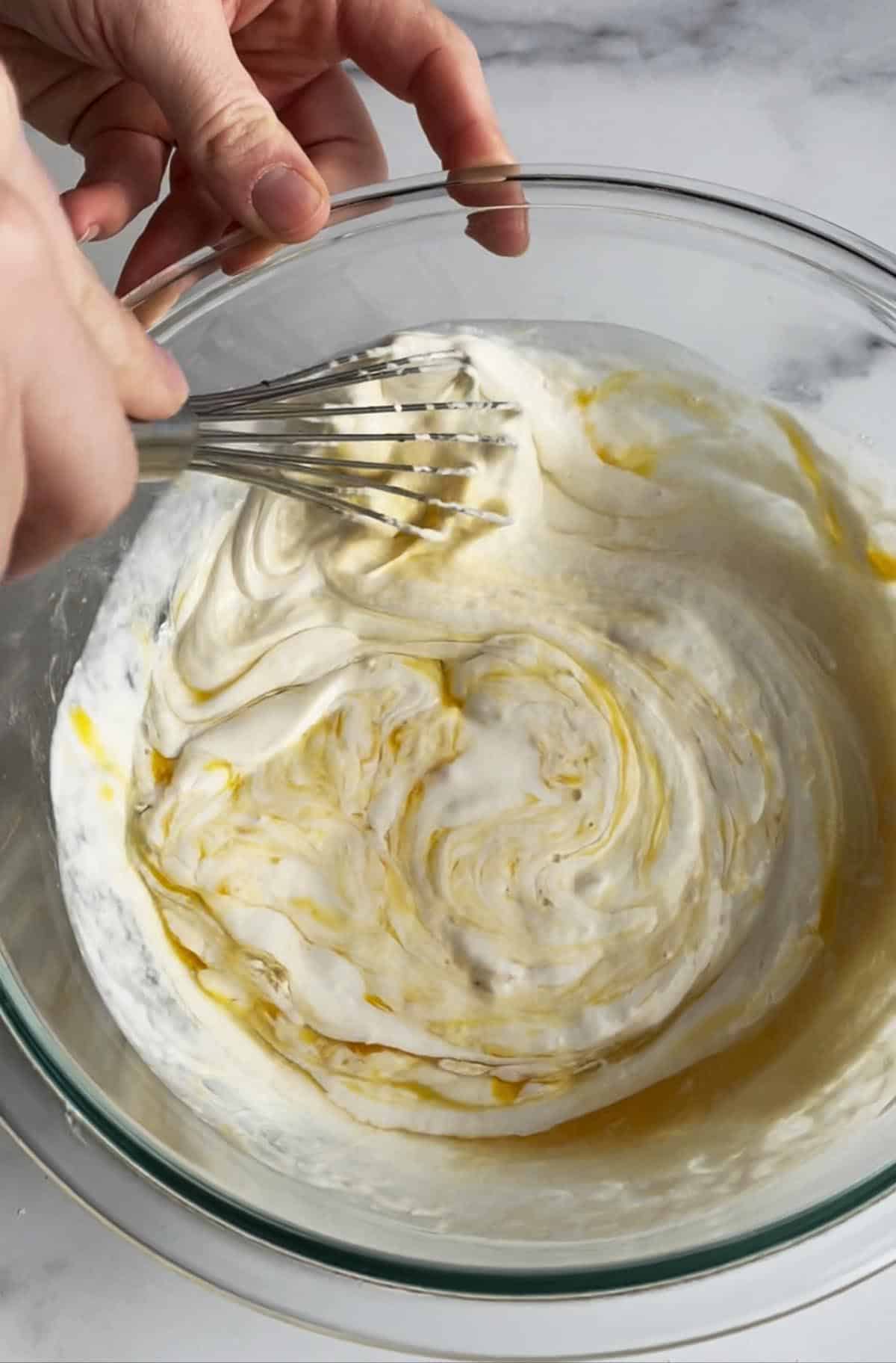 A glass bowl with a whisk mixing egg and vanilla extract.
