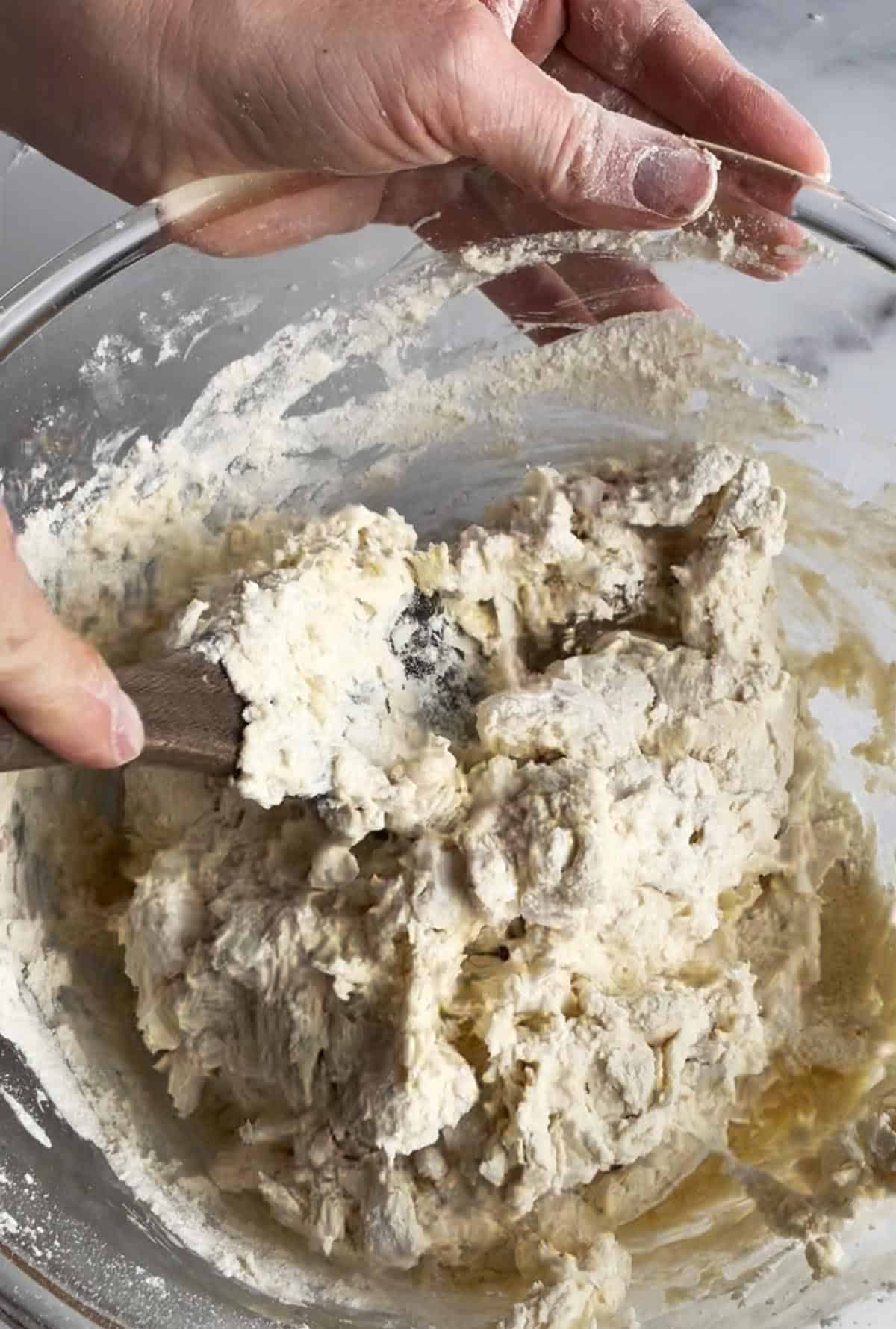 A glass bowl and wooden spoon mixing together scone dough.