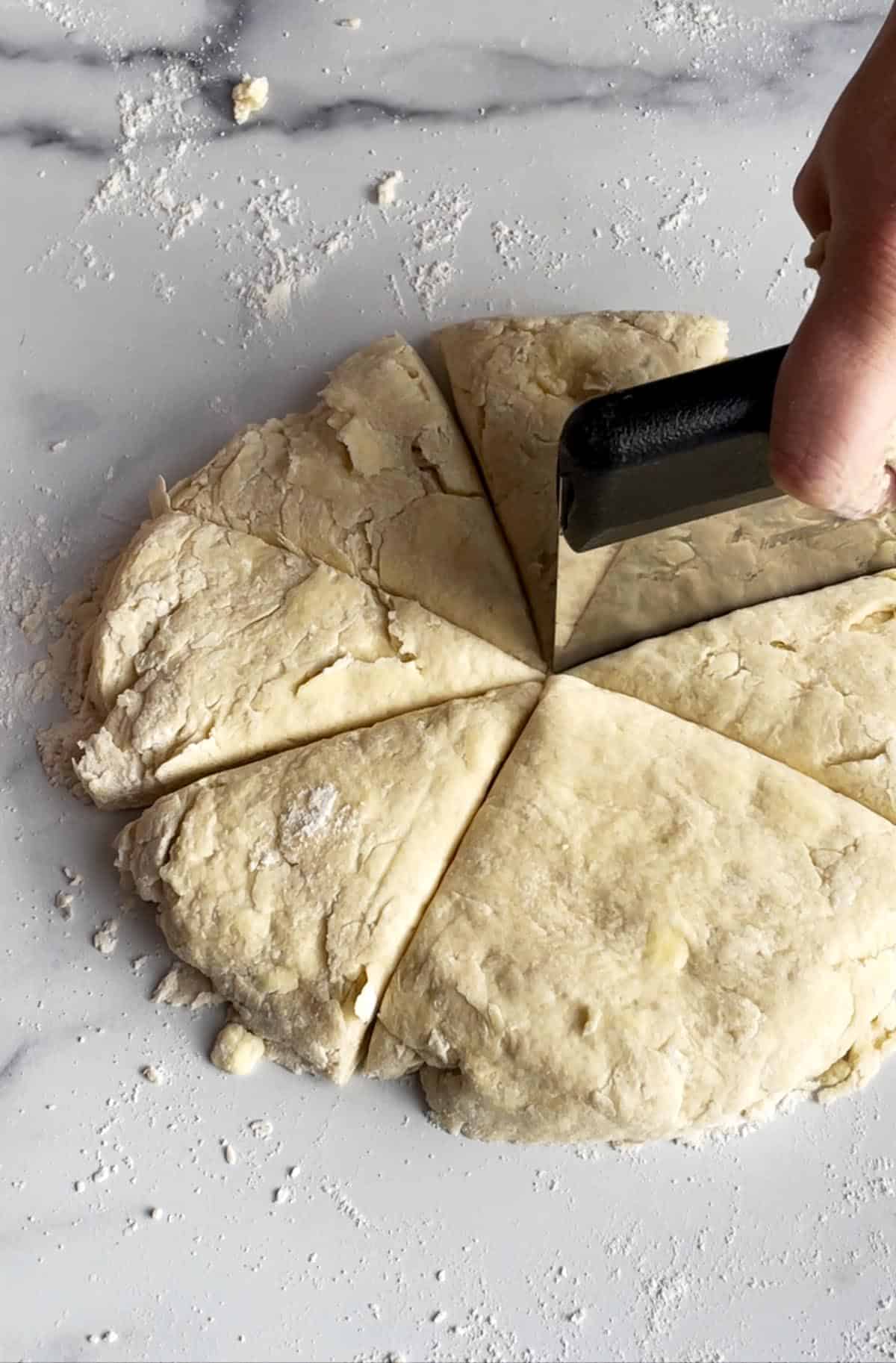 A bench scraper cutting scone dough into eight triangles. 