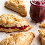 Scones with a jar of raspberry jam and one scone with jam inside.
