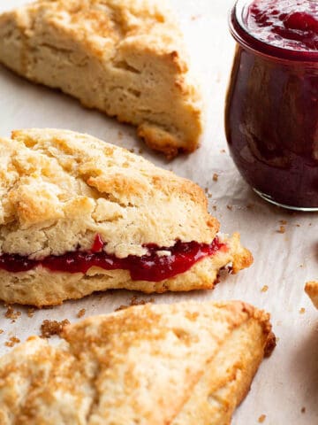 Scones with a jar of raspberry jam and one scone with jam inside.