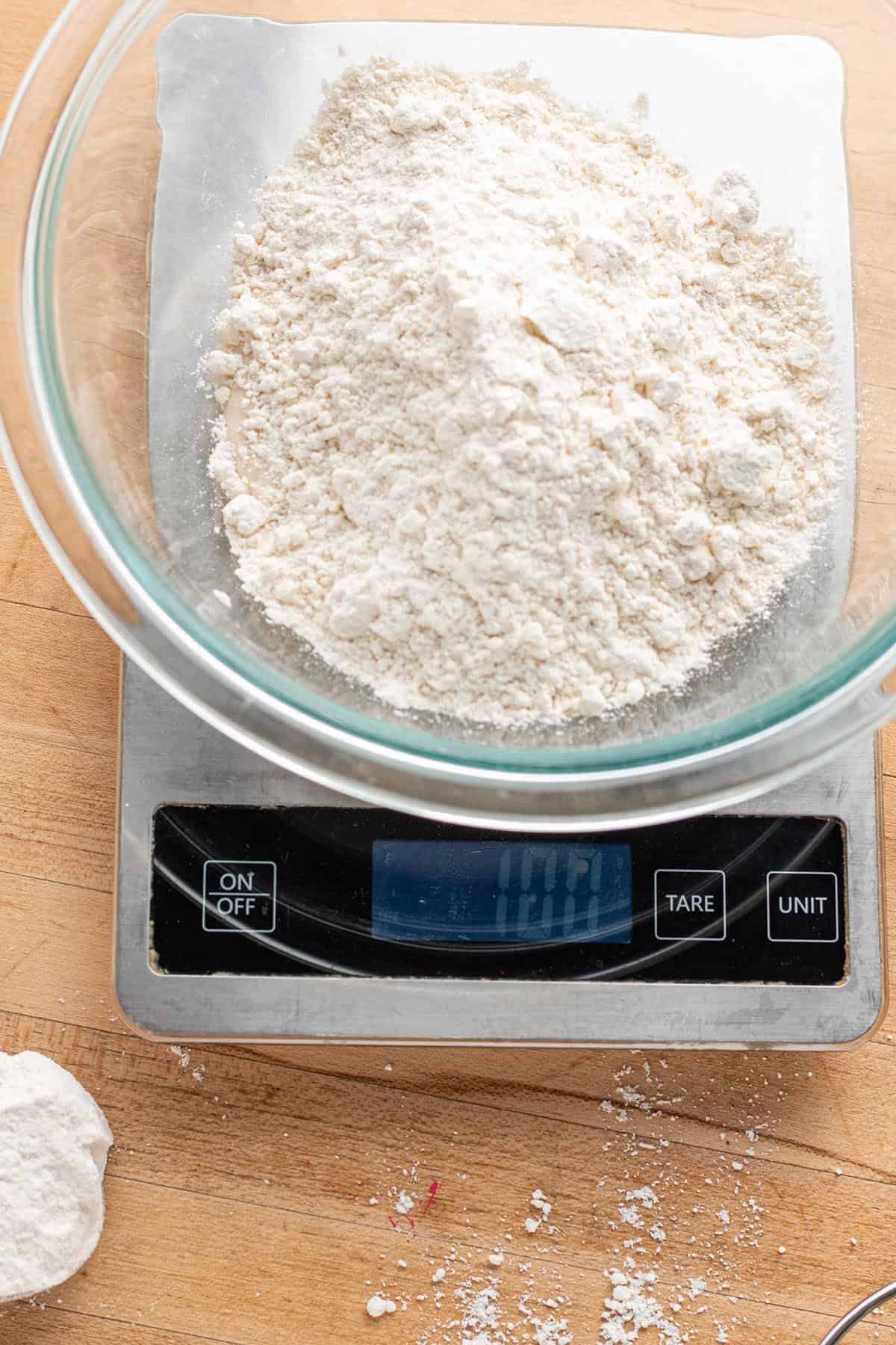 A digital scale measuring out 100grams of flour in a glass bowl.