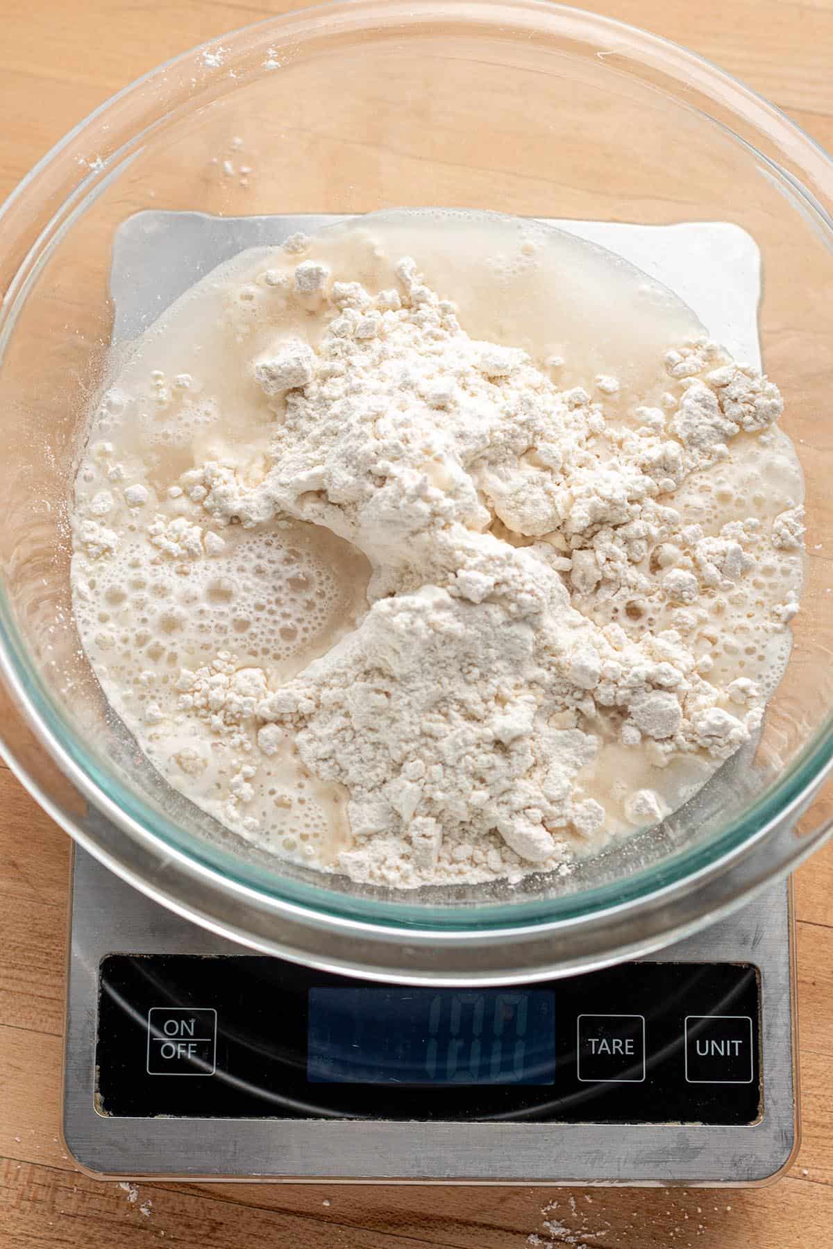 A digital scale measuring out 100 grams of water in a glass bowl.