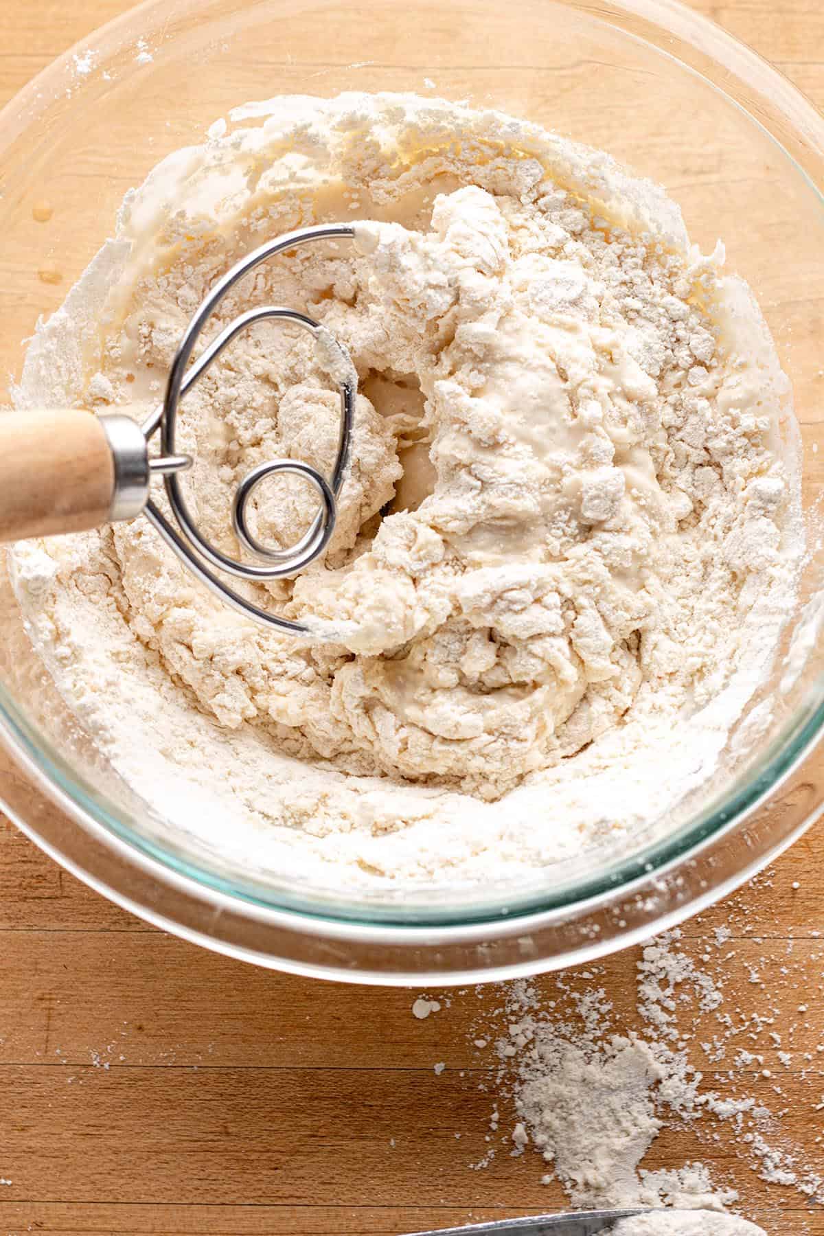 A glass bowl with a danish dough whisk mixing up a sourdough starter.