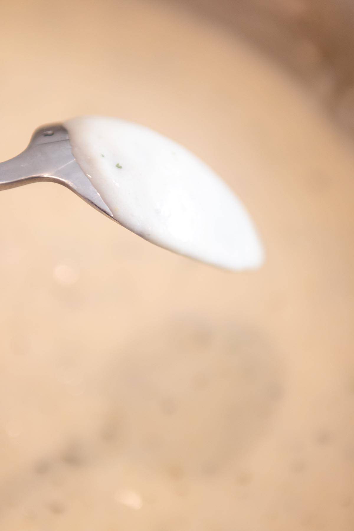 A metal spoon with a coating of a creamy roux on the back of it.