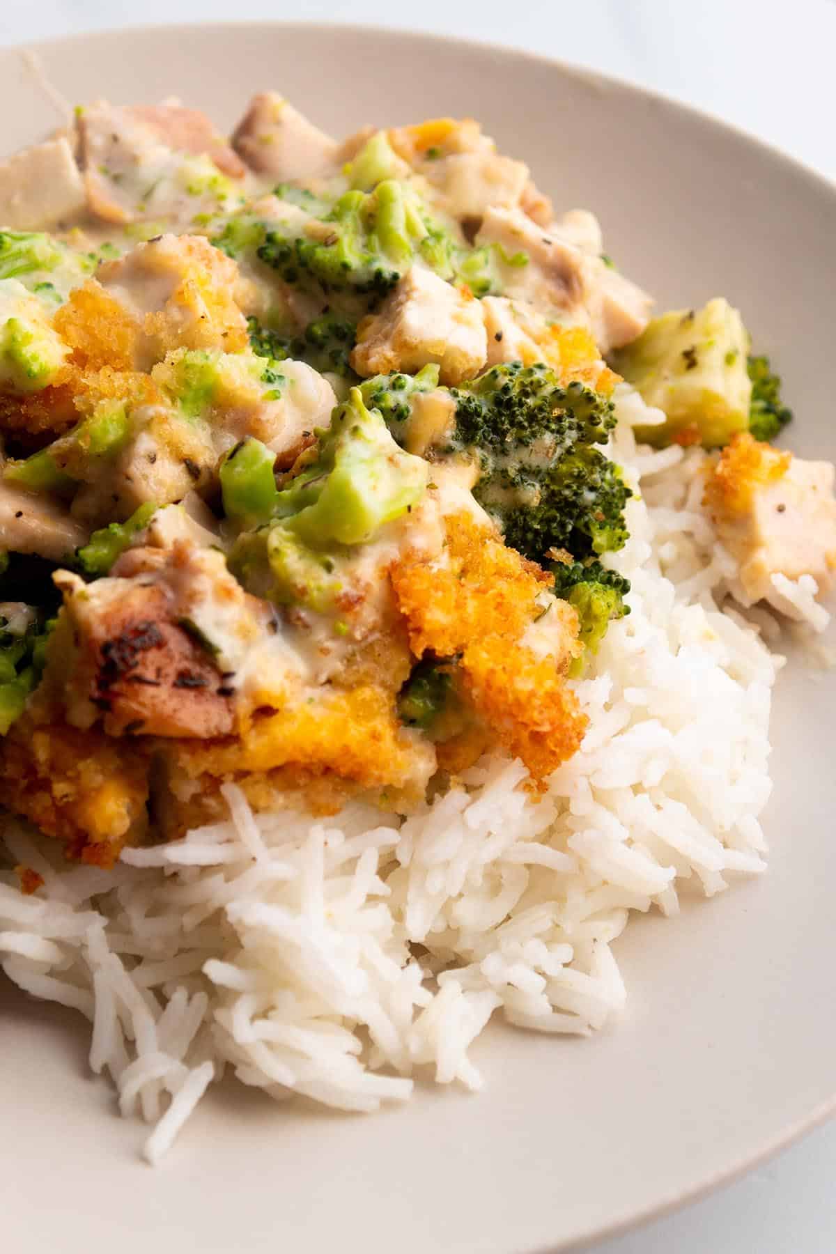 A plate with white rice then topped with a cheesy broccoli and turkey mix. 