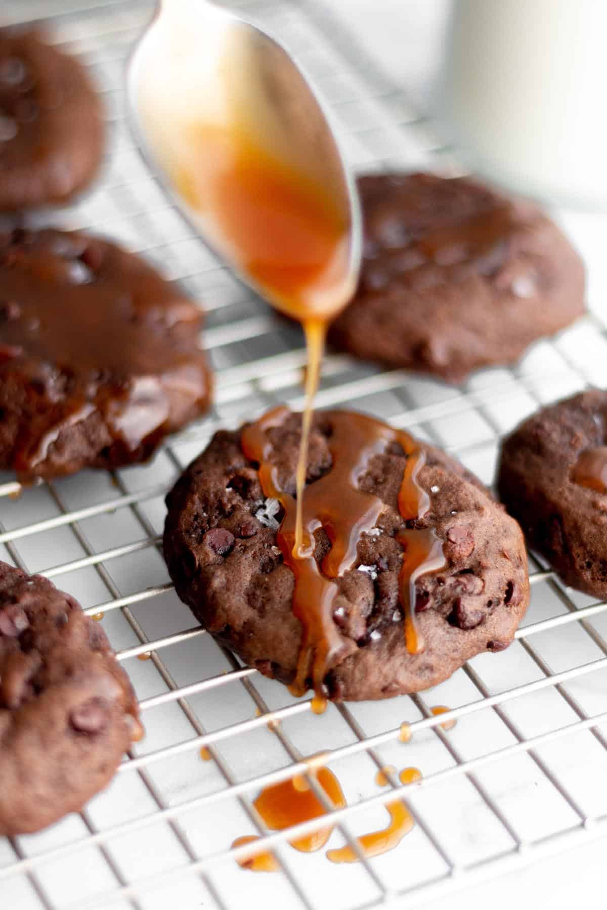 A cooling rack with chocolate cookies with caramel sauce being drizzled on top.