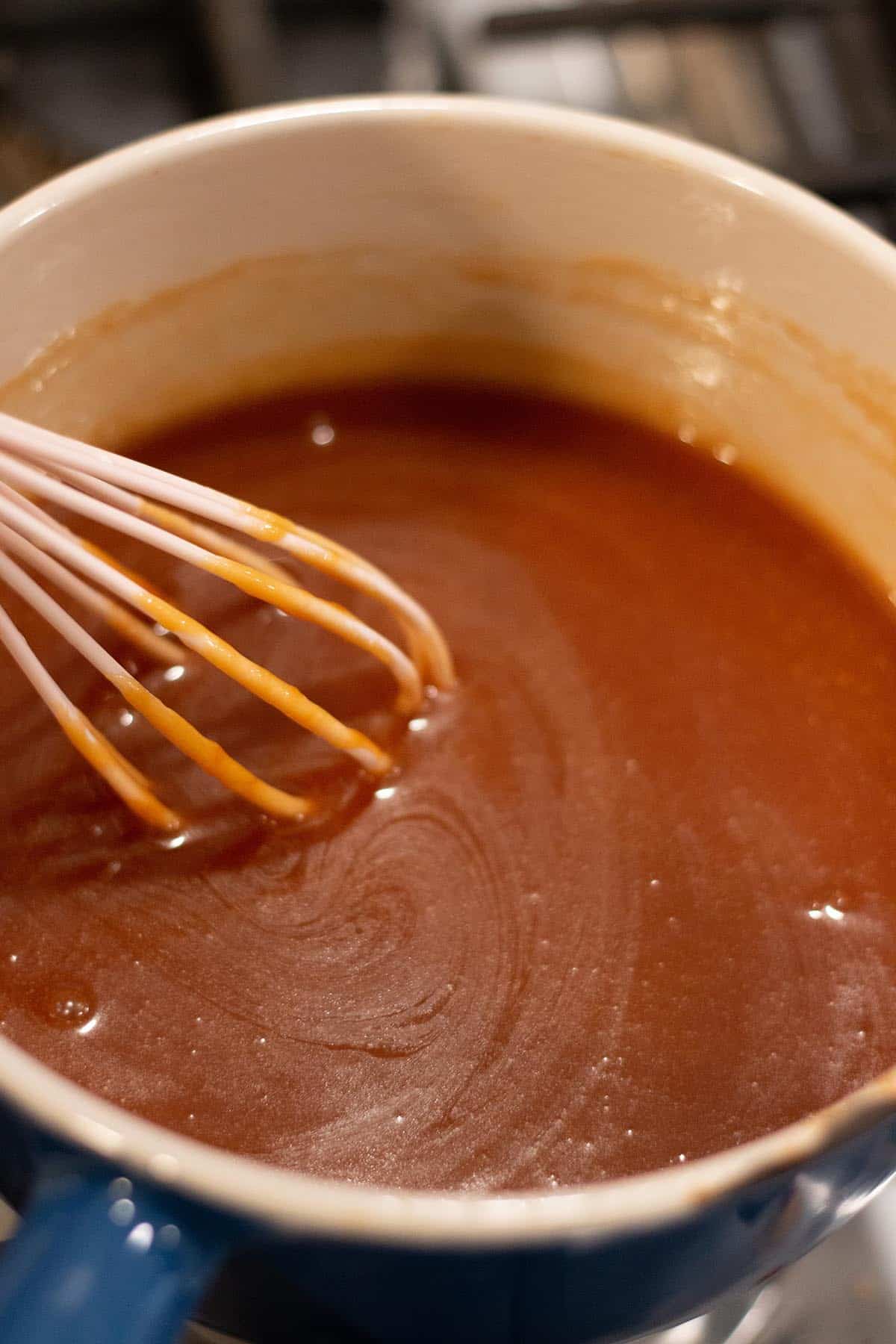 A small sauce pot with a caramel sauce being stored by a whisk.