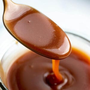 A spoon scooping out some caramel sauce out of a glass jar
