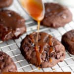 A wire cooling rack with chocolate cookies and caramel sauce being drizzled on top.