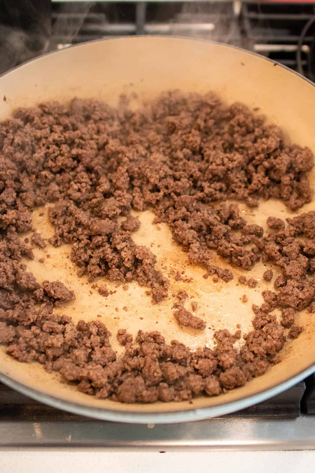 A large braiser with cooked ground beef. 