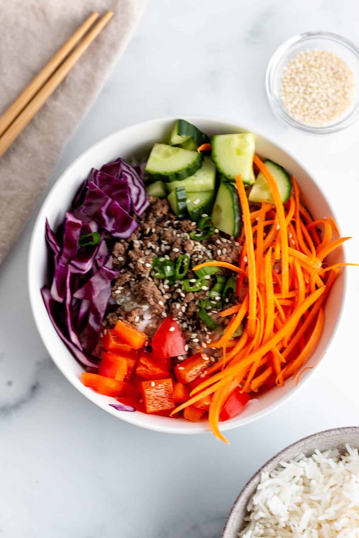 A bowl with julienne carrots, chopped peppers, cabbage, green onion and cooked ground beef.