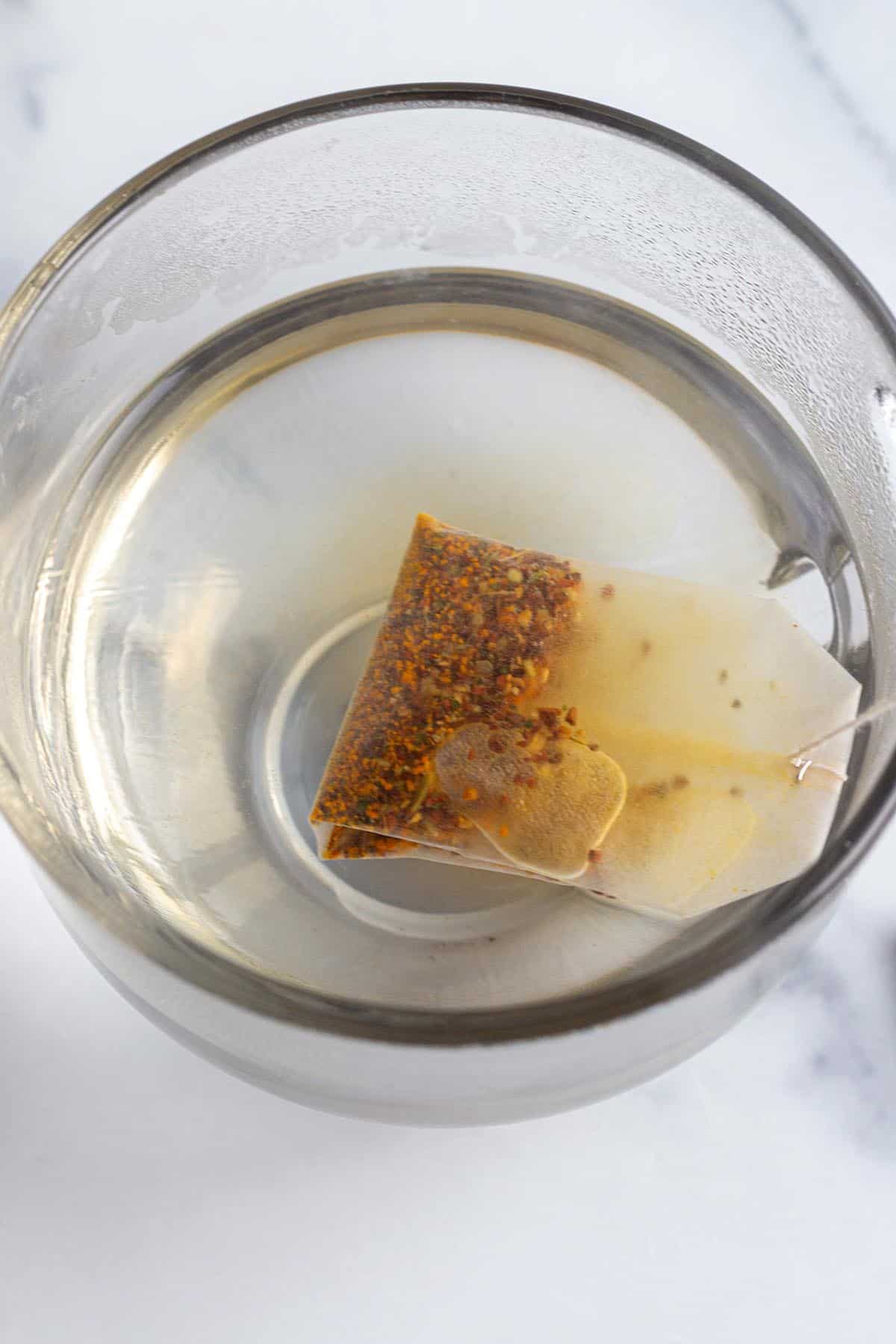 A glass mug with hot water and a tea bag steeping.