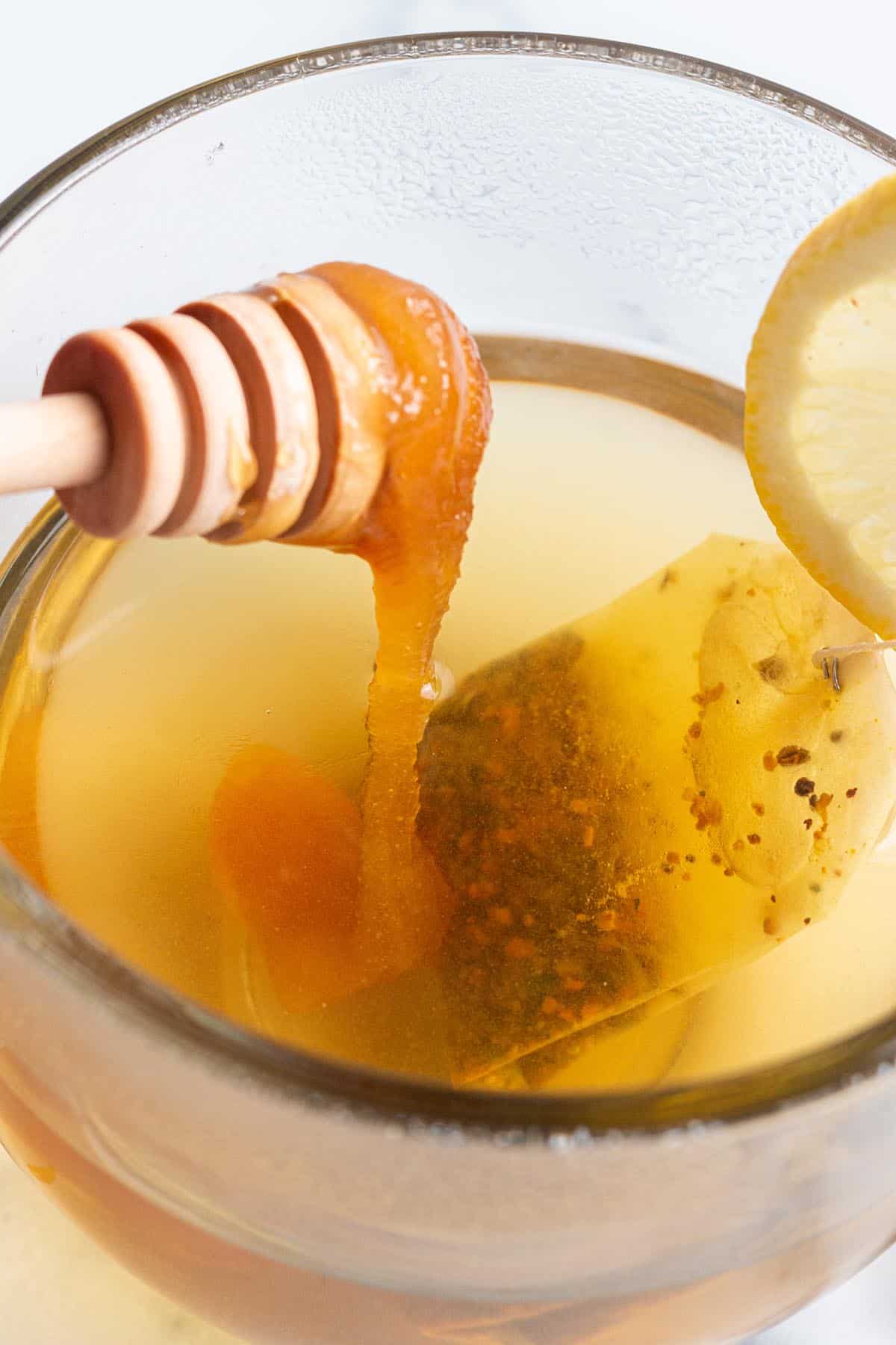 A glass mug with tea and honey being drizzled in.