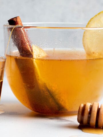 A glass mug with a tea, cinnamon stick and lemon slice.