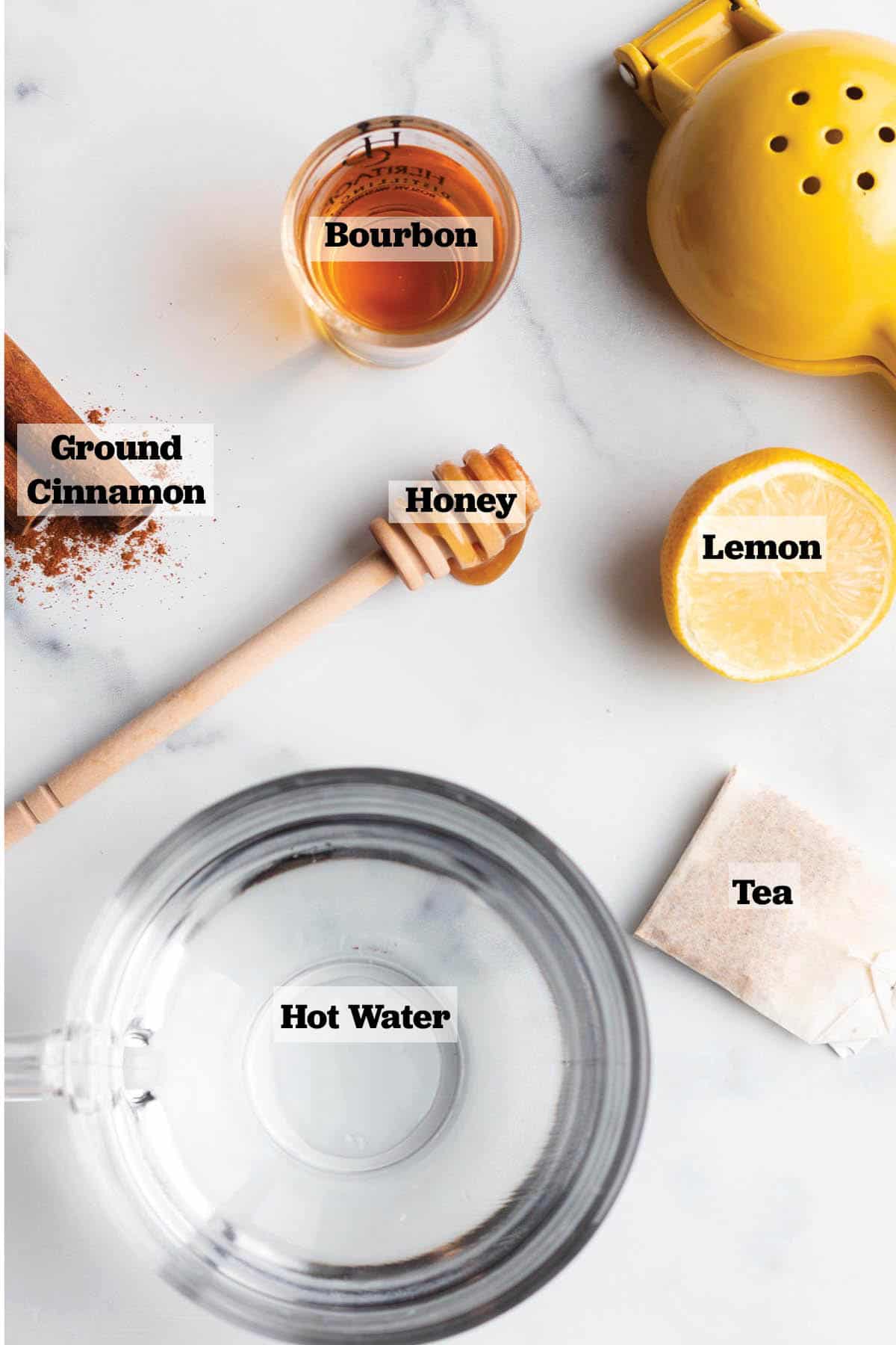 Ingredients to make a tea hot toddy. Hot water, tea bag, lemon, cinnamon, bourbon and honey stick.