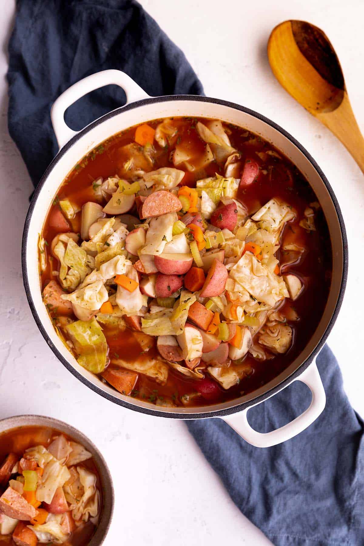 A white dutch oven with a potato, cabbage and sausage soup.