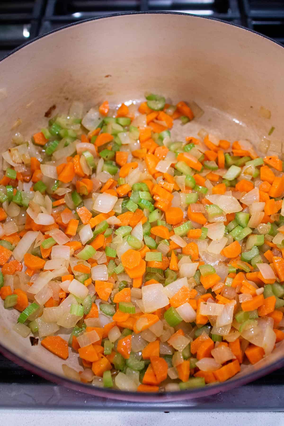 A large Dutch Oven with onions, carrots and celery being sautéed in olive oil.