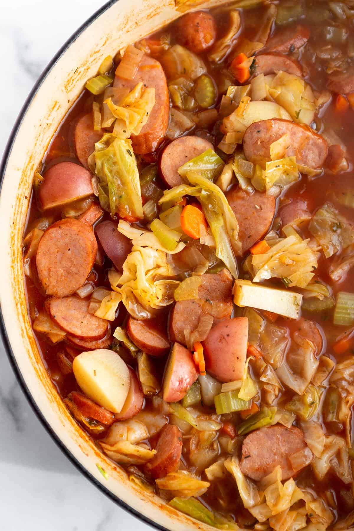 A large Dutch Oven with a soup made out of sausage, potatoes, cabbage and other veggies. 