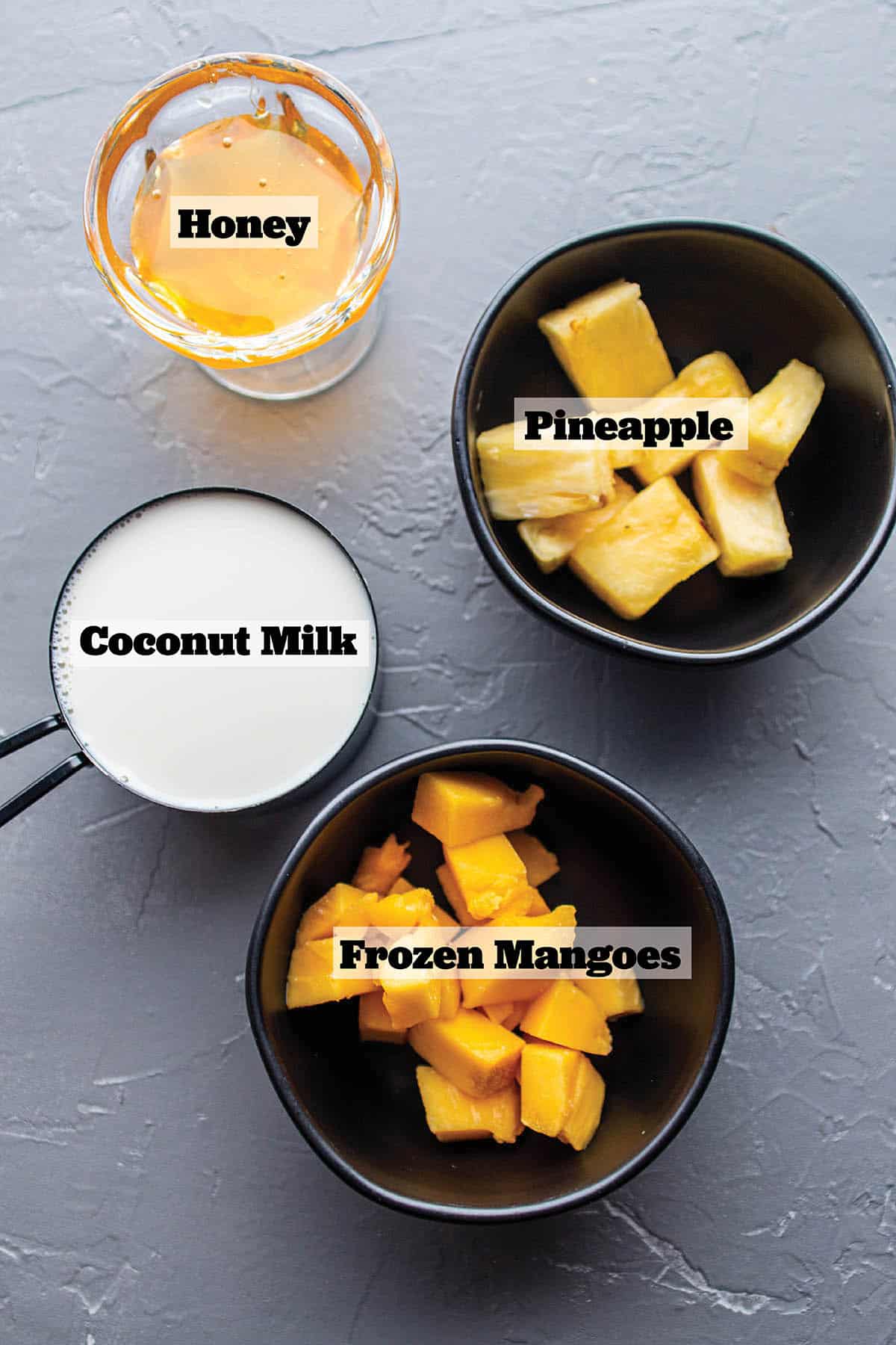 Black bowls with frozen mangoes, pineapple, coconut milk and honey.
