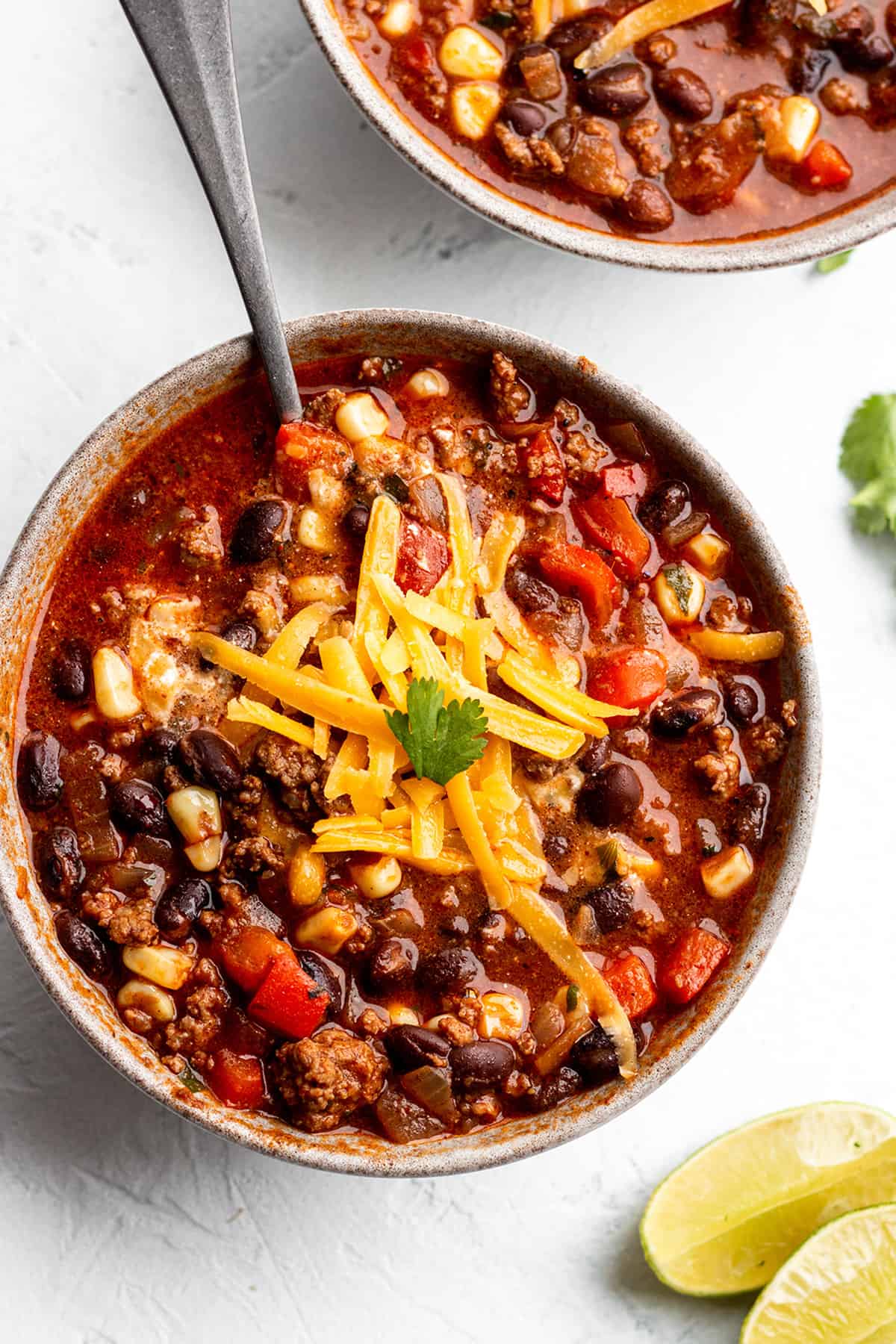 A small bowl with a soup made of beef, black beans, corn with cheddar cheese on top.