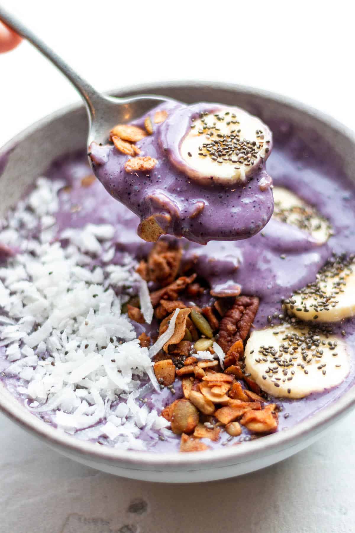 A spoon scooping out a purple smoothie with a banana, chai seeds and granola.