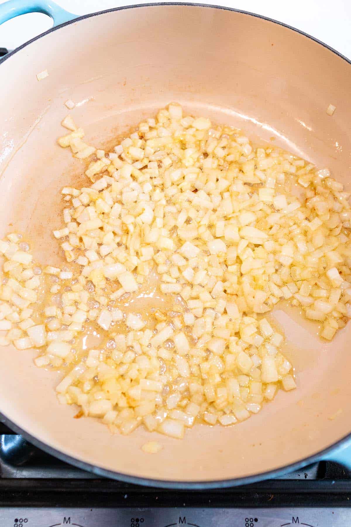 A large braiser pan with onions sautéing in butter and oil.
