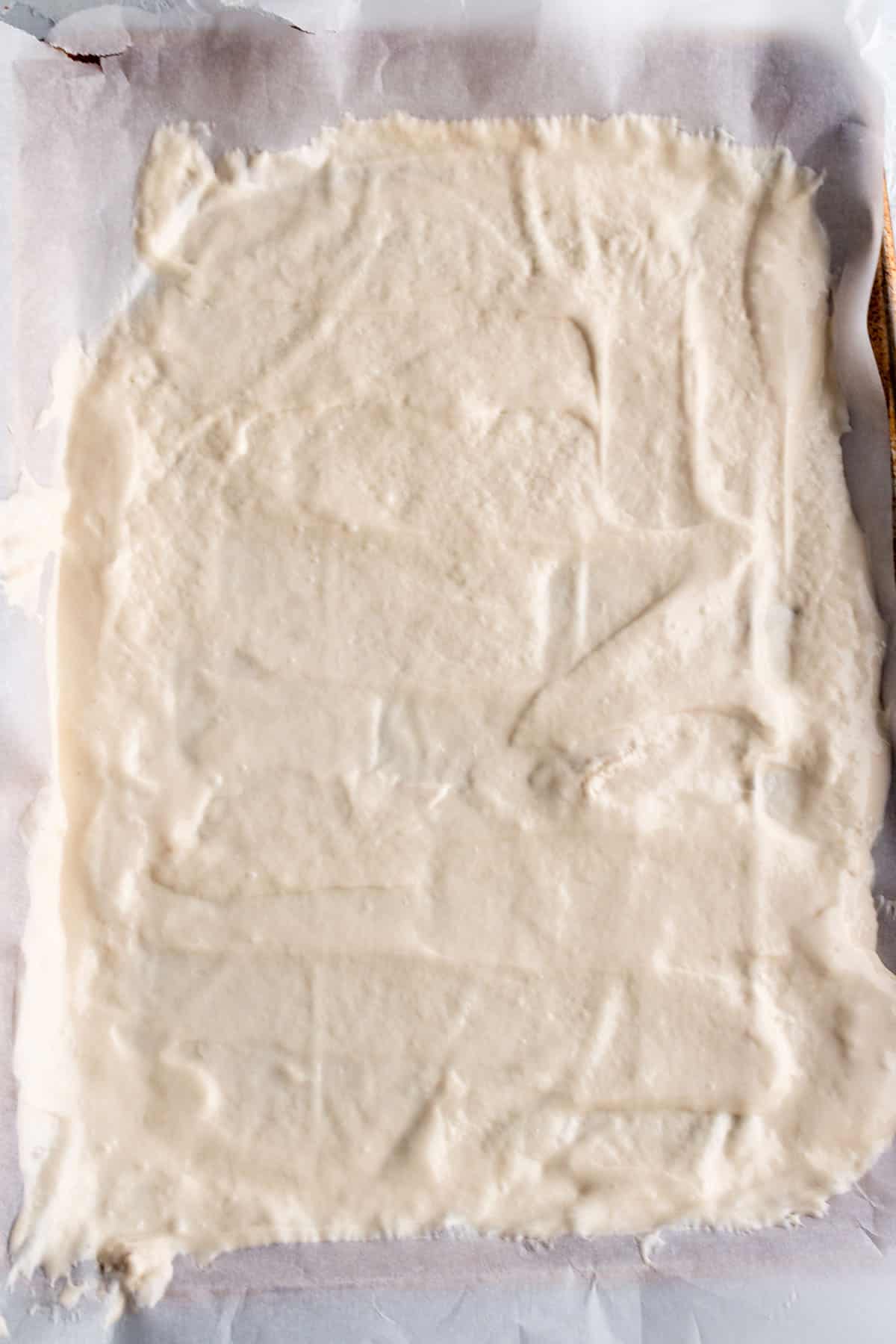 Baking sheet with parchment paper and sourdough starter spread out.
