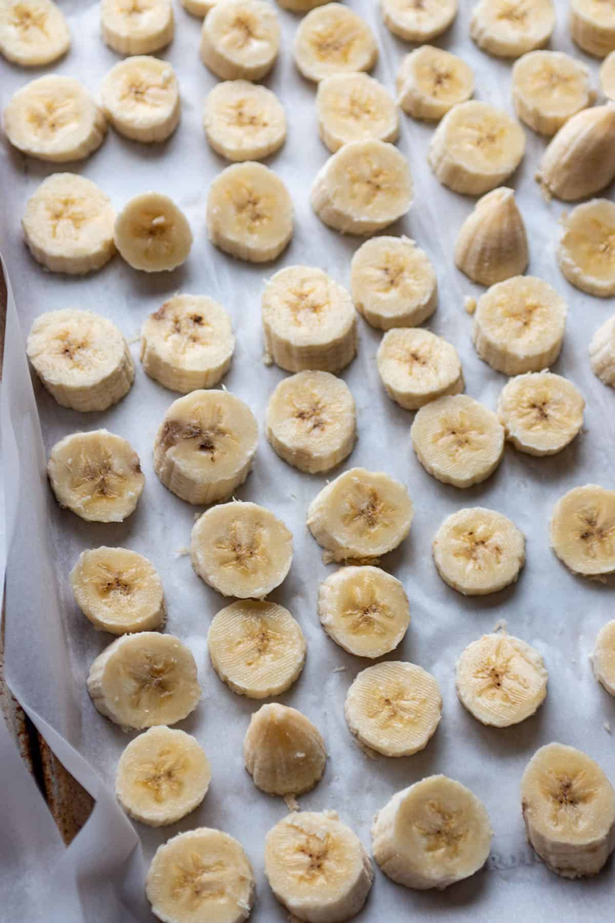 A baking sheet with some parchment paper and sliced of bananas. 